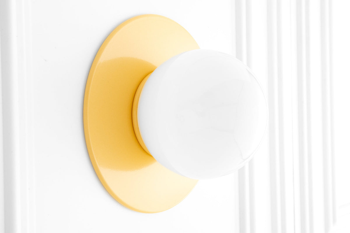 Yellow Scandinavian-style wall sconce with matte metal backplate and frosted globe light bulb. - SCONCE MODEL NO. 2277