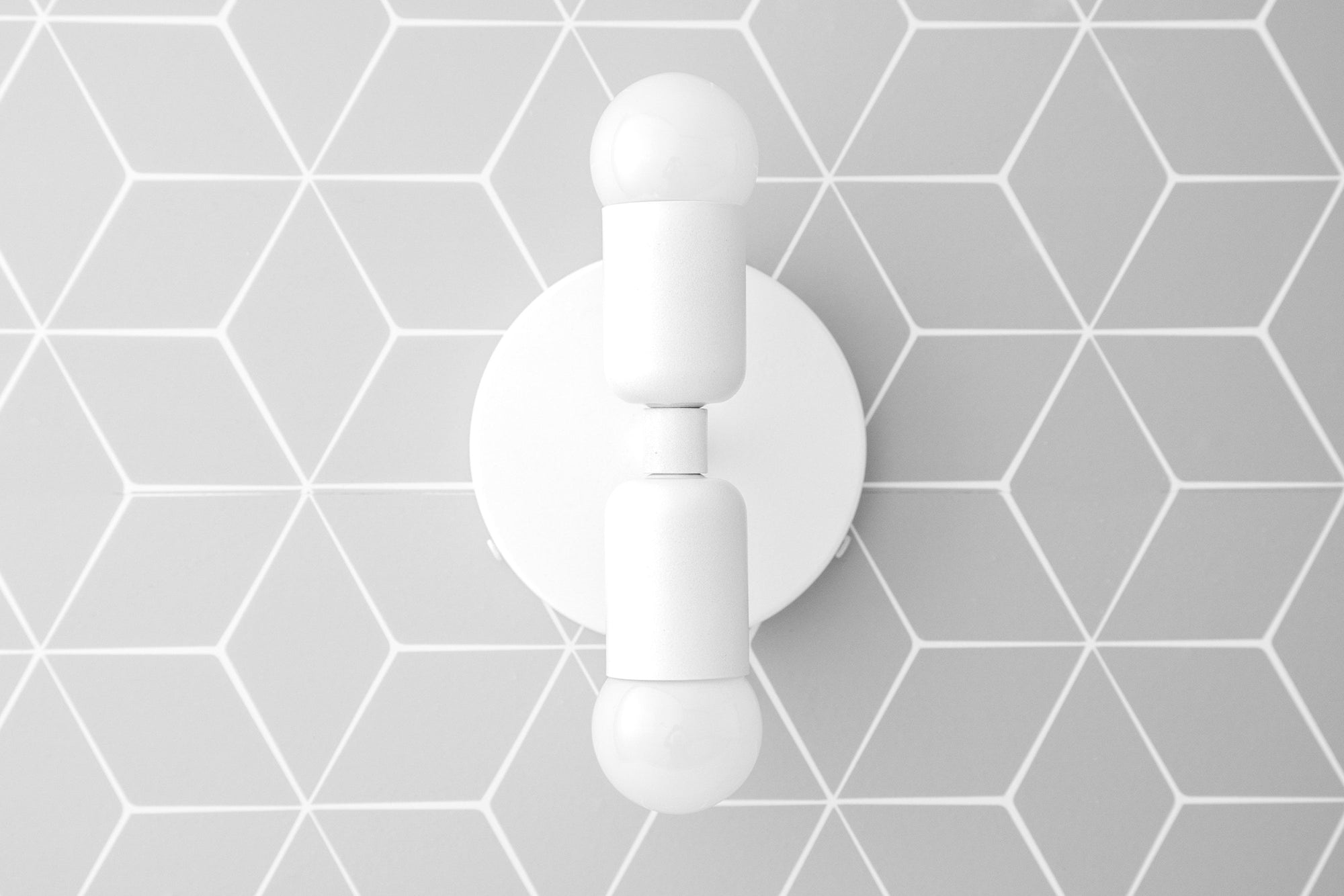 White double-bulb sconce with round backplate mounted on gray hexagonal tile wall. - SCONCE MODEL NO. 2660