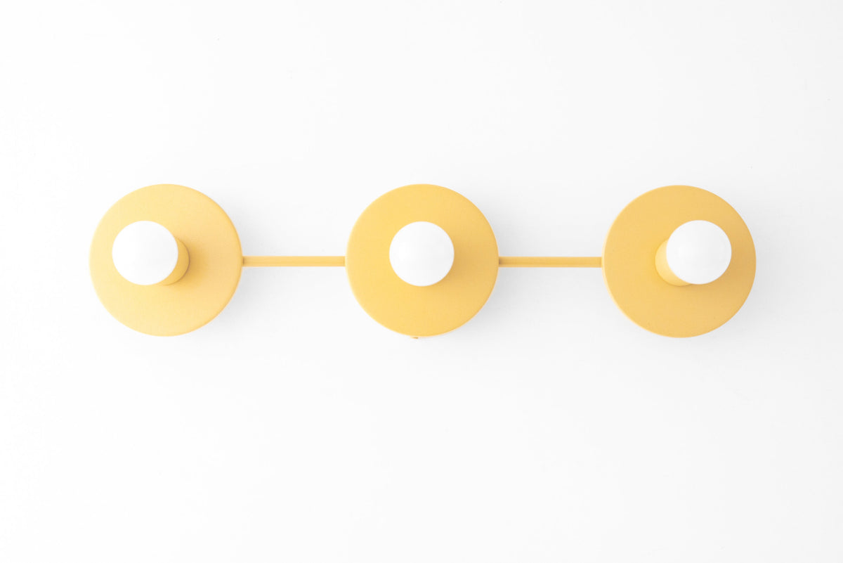 Mid-century modern vanity light with three round yellow metal backplates and bare bulbs mounted on horizontal bar. - VANITY LIGHT MODEL NO. 5708