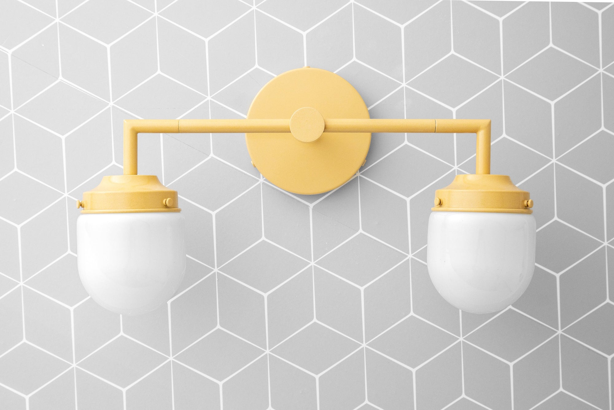 Two-bulb vanity light with yellow metal frame and frosted white glass globes on geometric gray tile background. - VANITY LIGHT MODEL NO. 7536