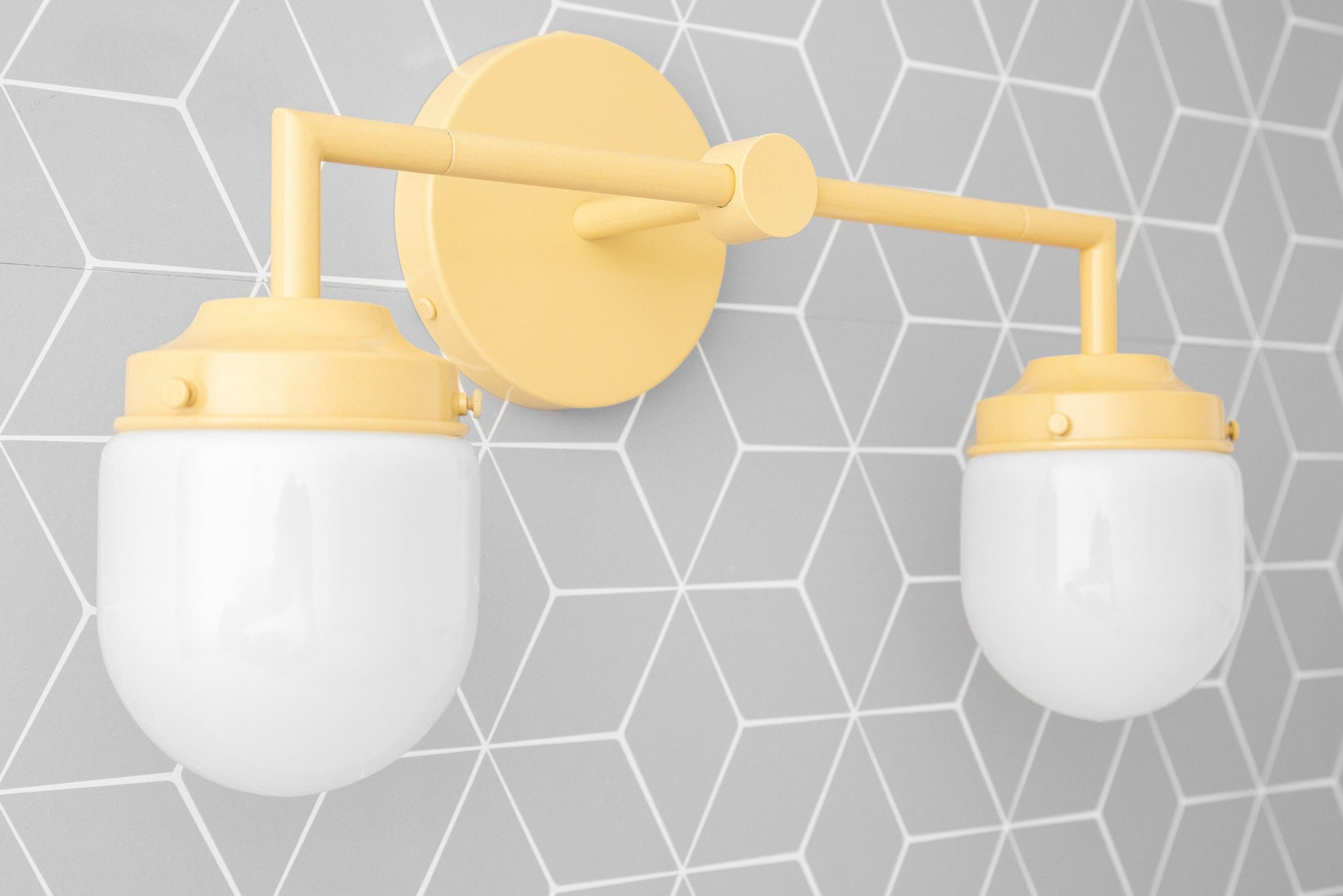 Yellow metal vanity light with two white globe bulbs mounted on gray hexagonal tile wall. - VANITY LIGHT MODEL NO. 7536