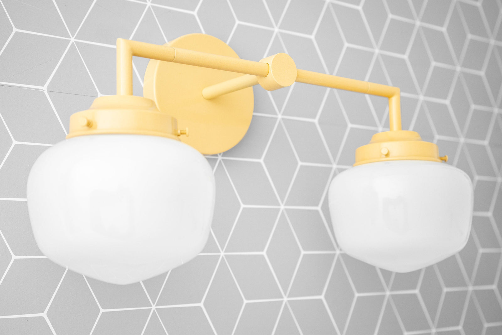 Cream-colored two-bulb vanity light with round glass globes and matte finish mount against gray geometric tile wall. - VANITY LIGHT MODEL NO. 0276