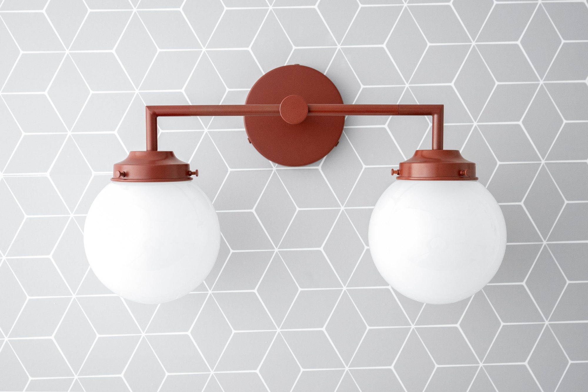 Brick red vanity light with two white globe bulbs and round wall mount on geometric gray tile background. - VANITY LIGHT MODEL NO. 9500