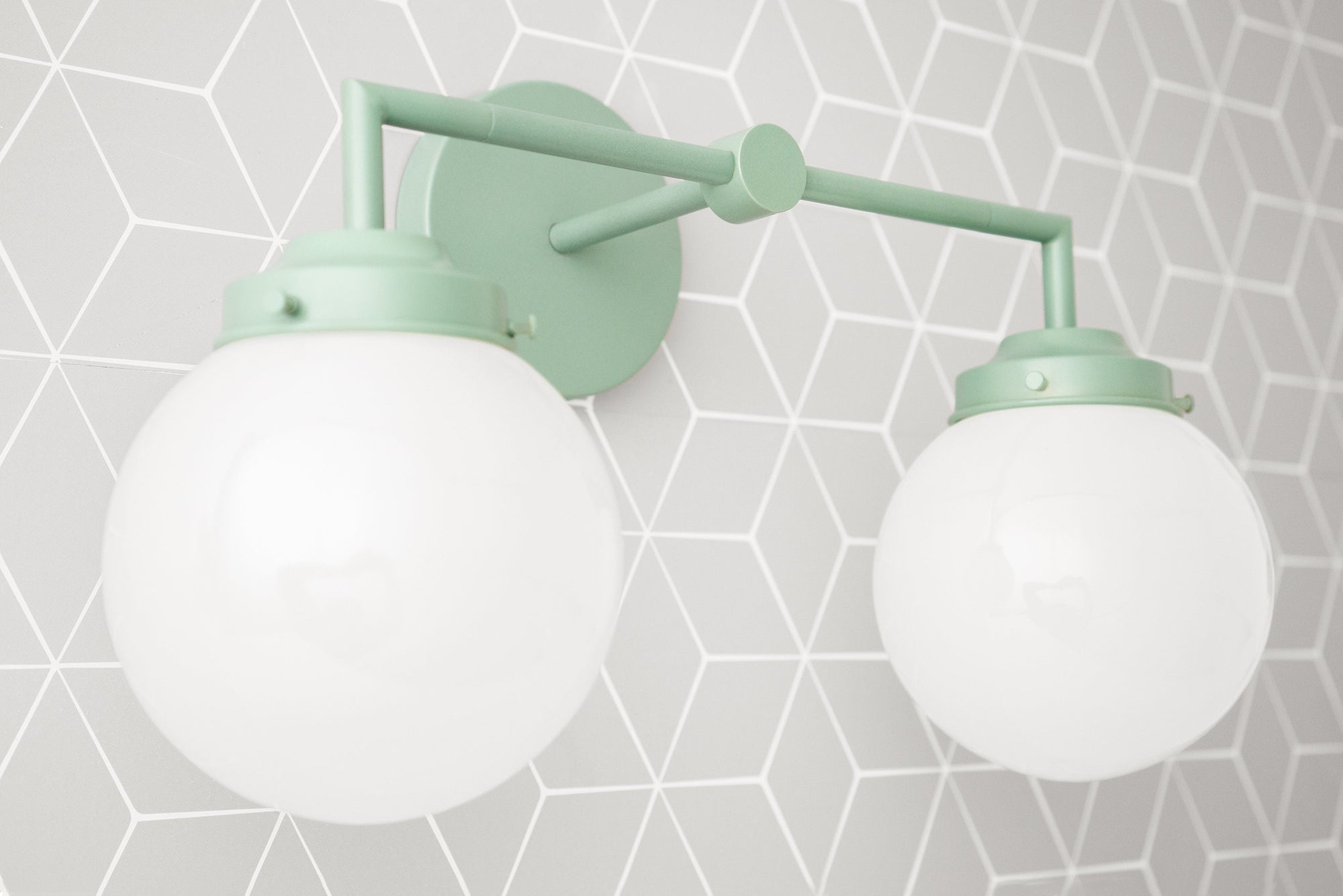 Vanity light with two white glass globes and matte green metal frame mounted on geometric gray wall. - VANITY LIGHT MODEL NO. 9500