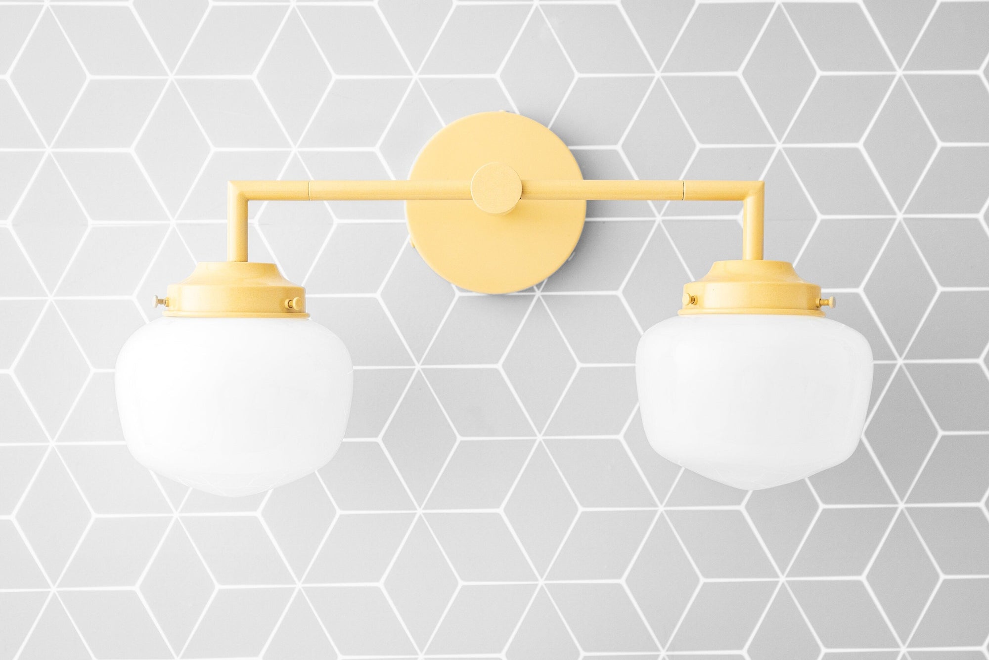 Yellow two-bulb vanity light with frosted globe shades and round wall mount on geometric gray wallpaper background. - VANITY LIGHT MODEL NO. 0276