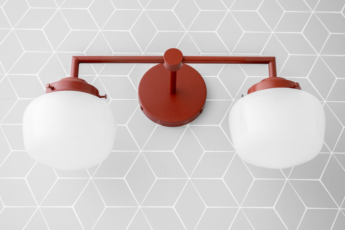 Art Deco style double globe vanity light in matte brick red finish against gray geometric tile background. - VANITY LIGHT MODEL NO. 0276