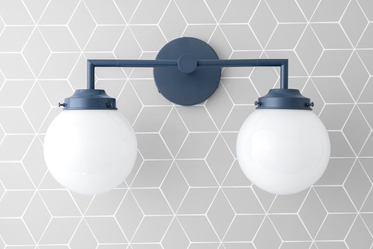 Two-bulb vanity light with coal blue metal frame and white globe shades on geometric gray tile wall. - VANITY LIGHT MODEL NO. 9500