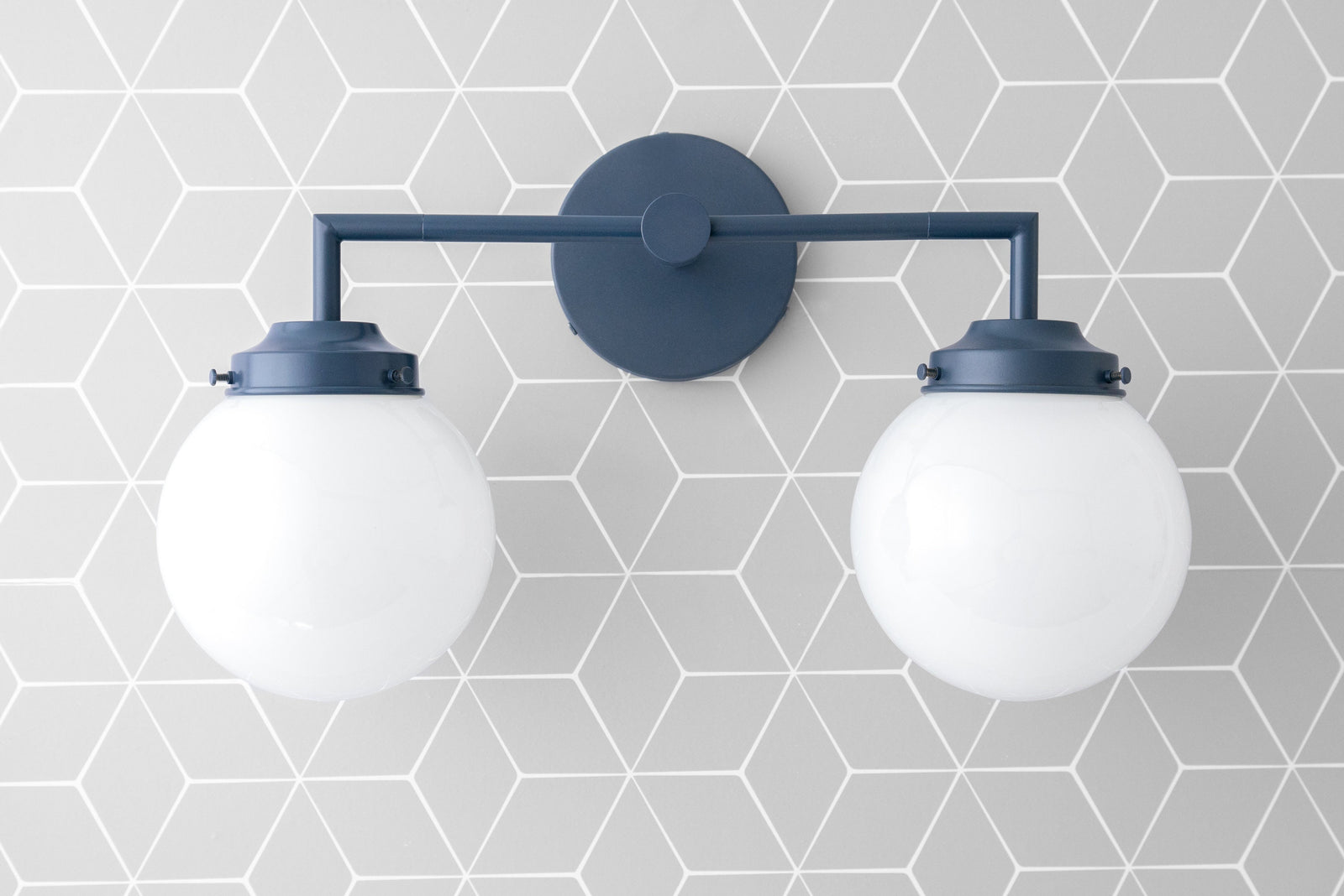 Two-bulb vanity light with coal blue metal frame and white globe shades on geometric gray tile wall. - VANITY LIGHT MODEL NO. 9500