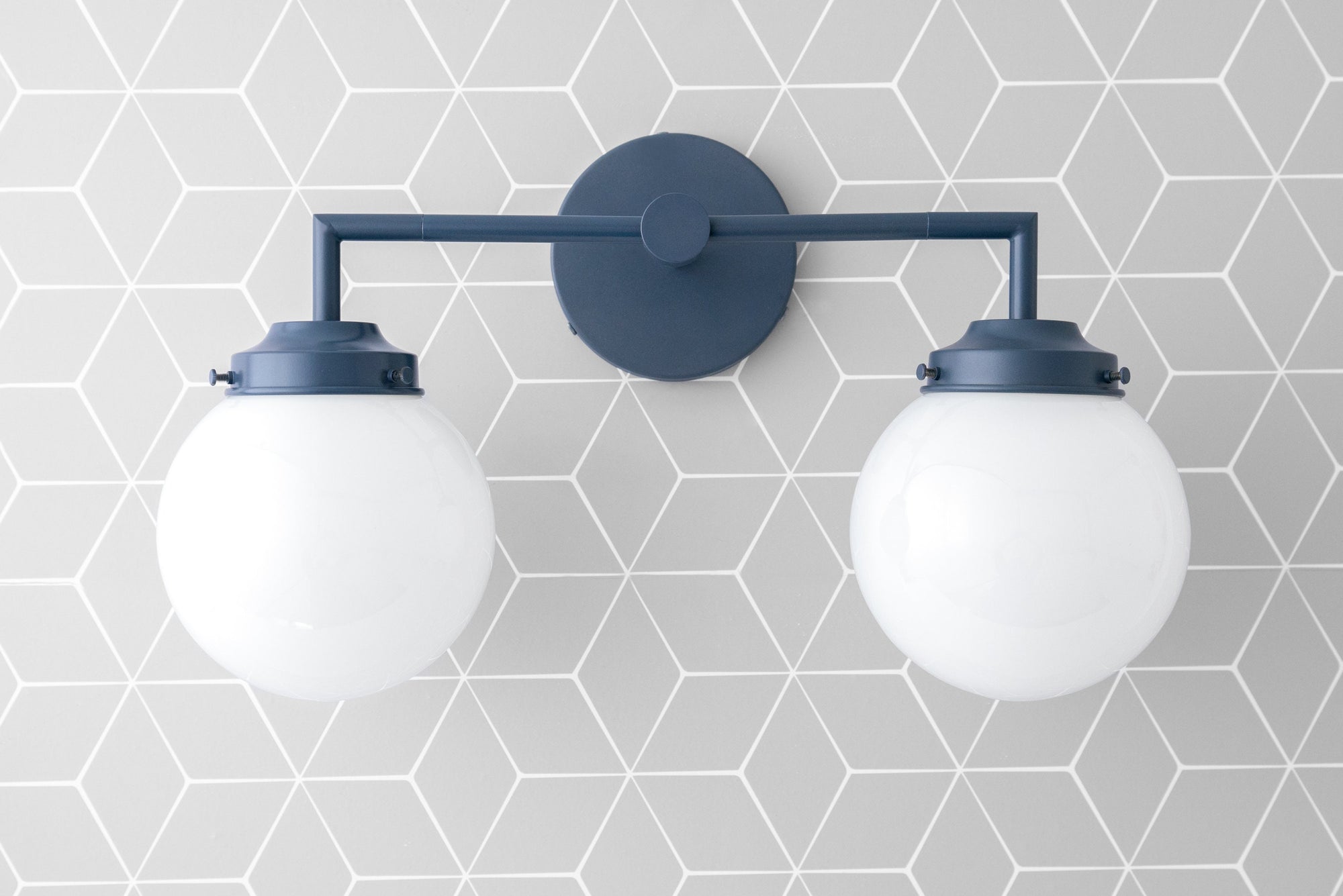 Two-bulb vanity light with coal blue metal frame and white globe shades on geometric gray tile wall. - VANITY LIGHT MODEL NO. 9500