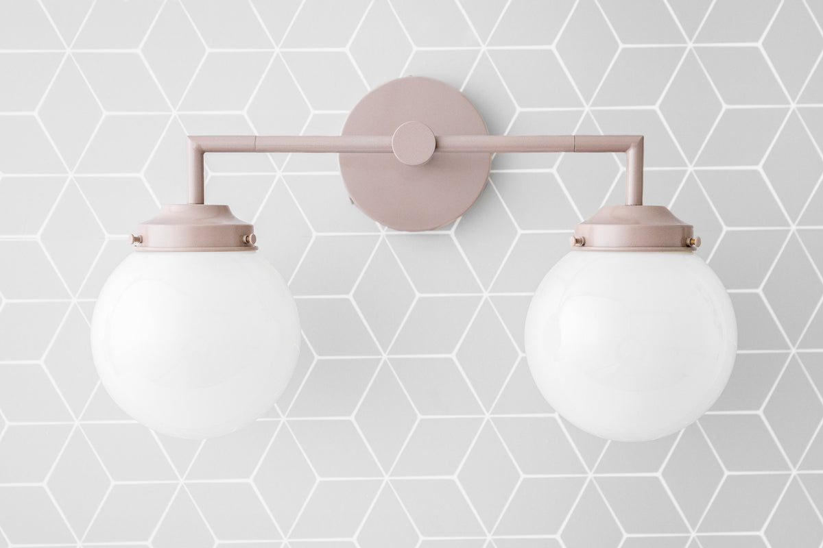 Mauve vanity light with two white globe bulbs mounted on geometric patterned wall. - VANITY LIGHT MODEL NO. 9500