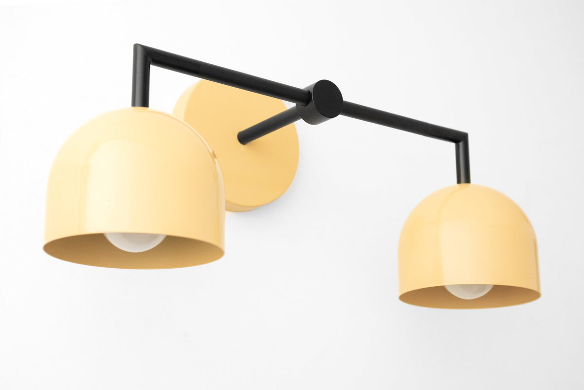 Art Deco two-bulb vanity light with matte black frame and soft yellow dome shades. - VANITY LIGHT MODEL NO. 8432