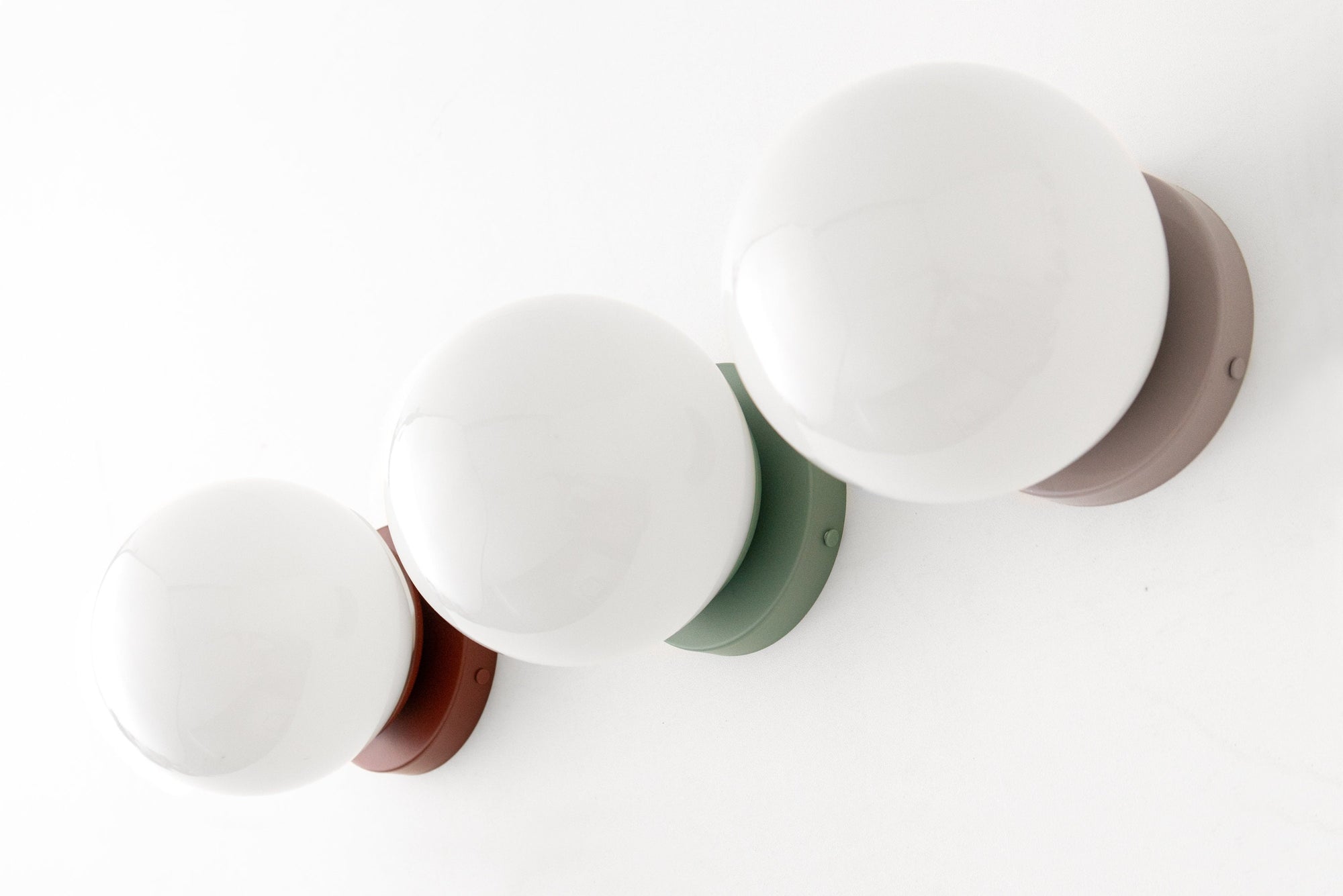 Set of four mid-century modern wall sconces with white globe shades and colored flush mounts in brick red, mauve, green, and . - SCONCE MODEL NO. 3825