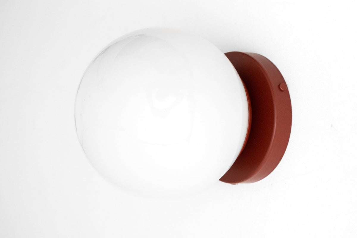 Mid-century modern wall sconce with a round white glass globe and a brick red flush mount base. - SCONCE MODEL NO. 3825