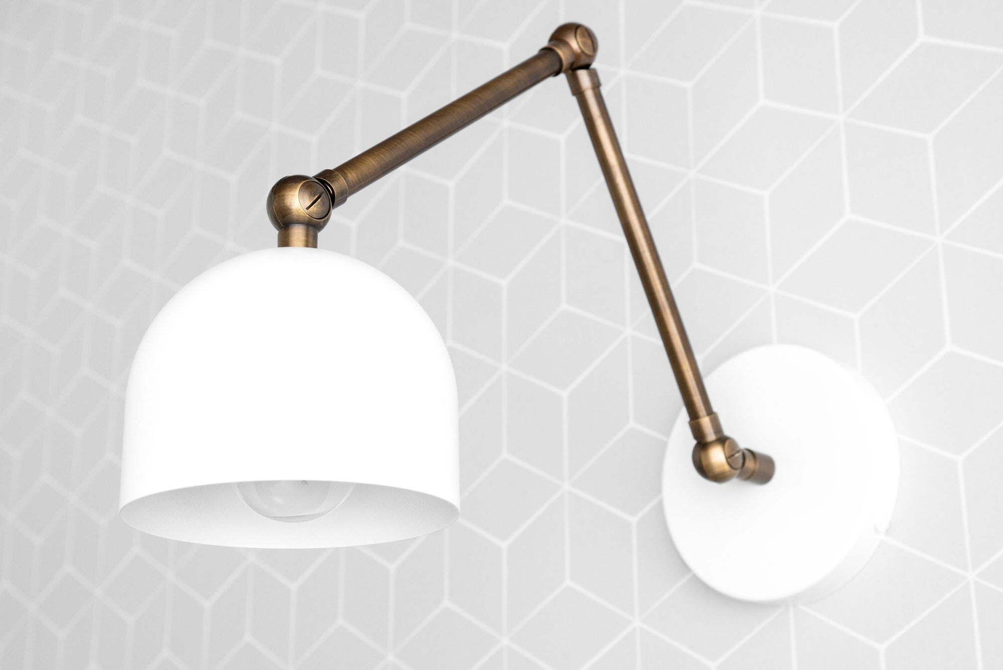 Antique brass adjustable wall sconce with smooth white dome shade and geometric background. - SCONCE MODEL NO. 5998