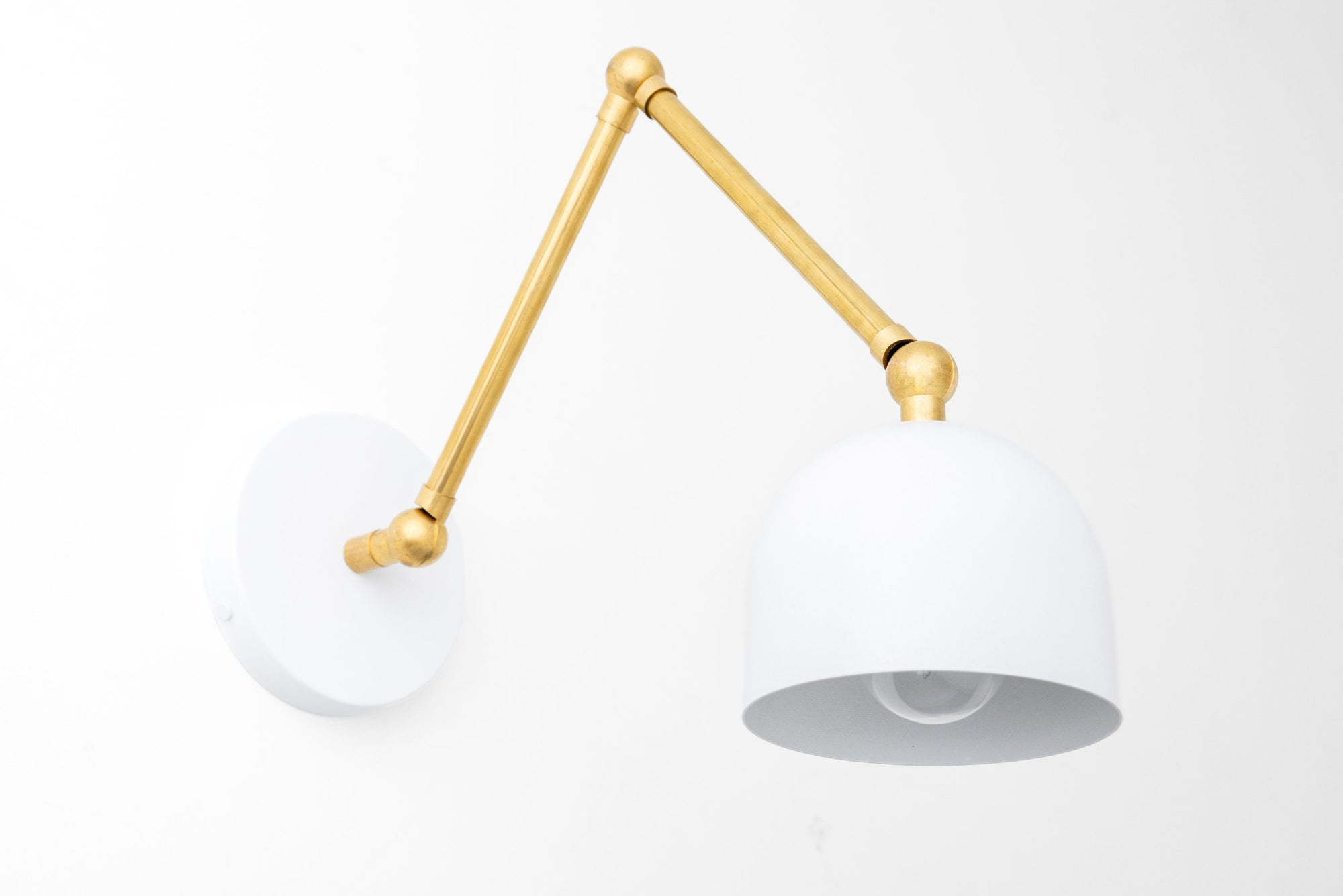 Adjustable industrial sconce with raw brass arm and white dome shade mounted on white wall plate. - SCONCE MODEL NO. 5998