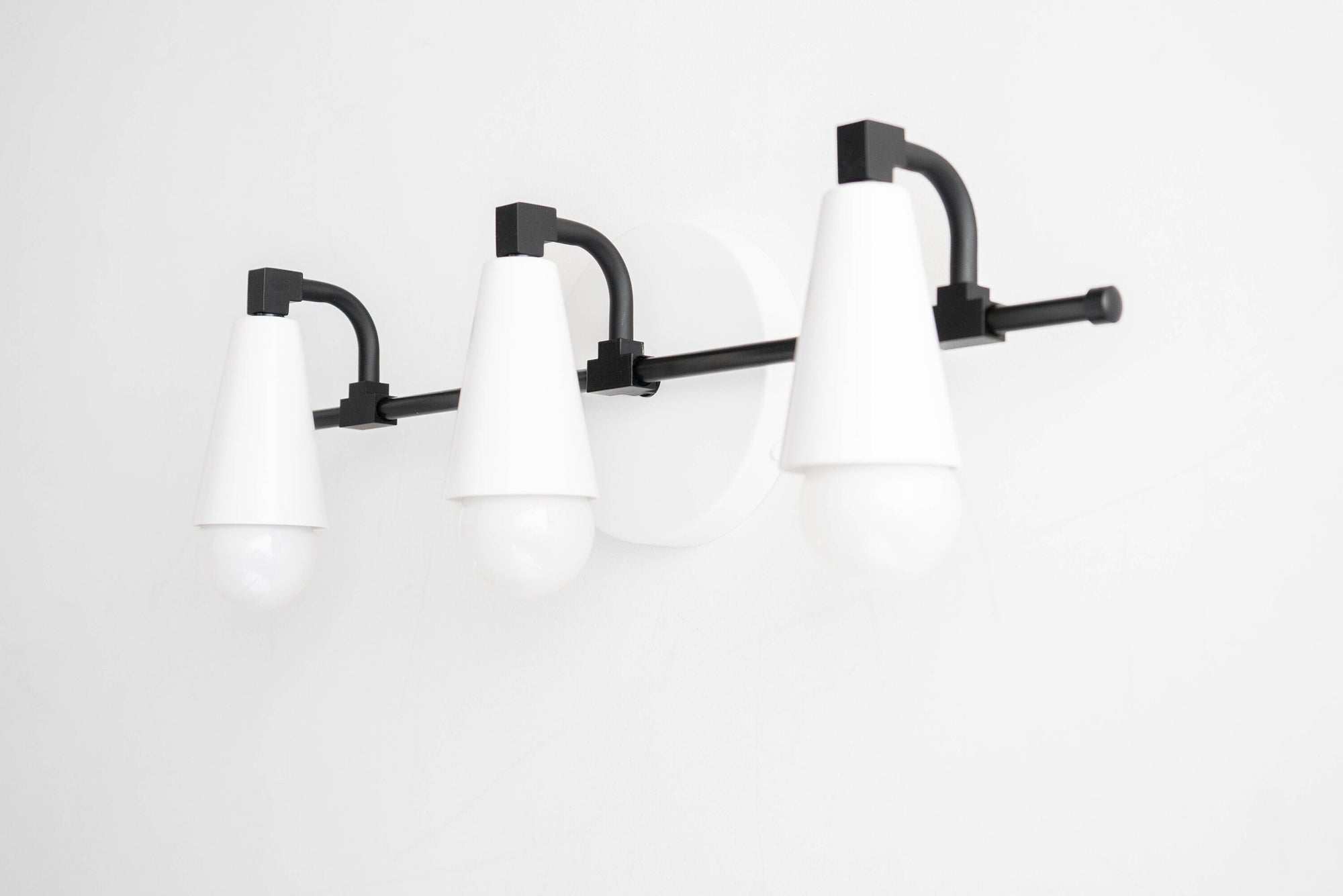 Mid-century modern vanity light with three white cone-shaped shades and black metal fixtures. - VANITY LIGHT MODEL NO. 8084