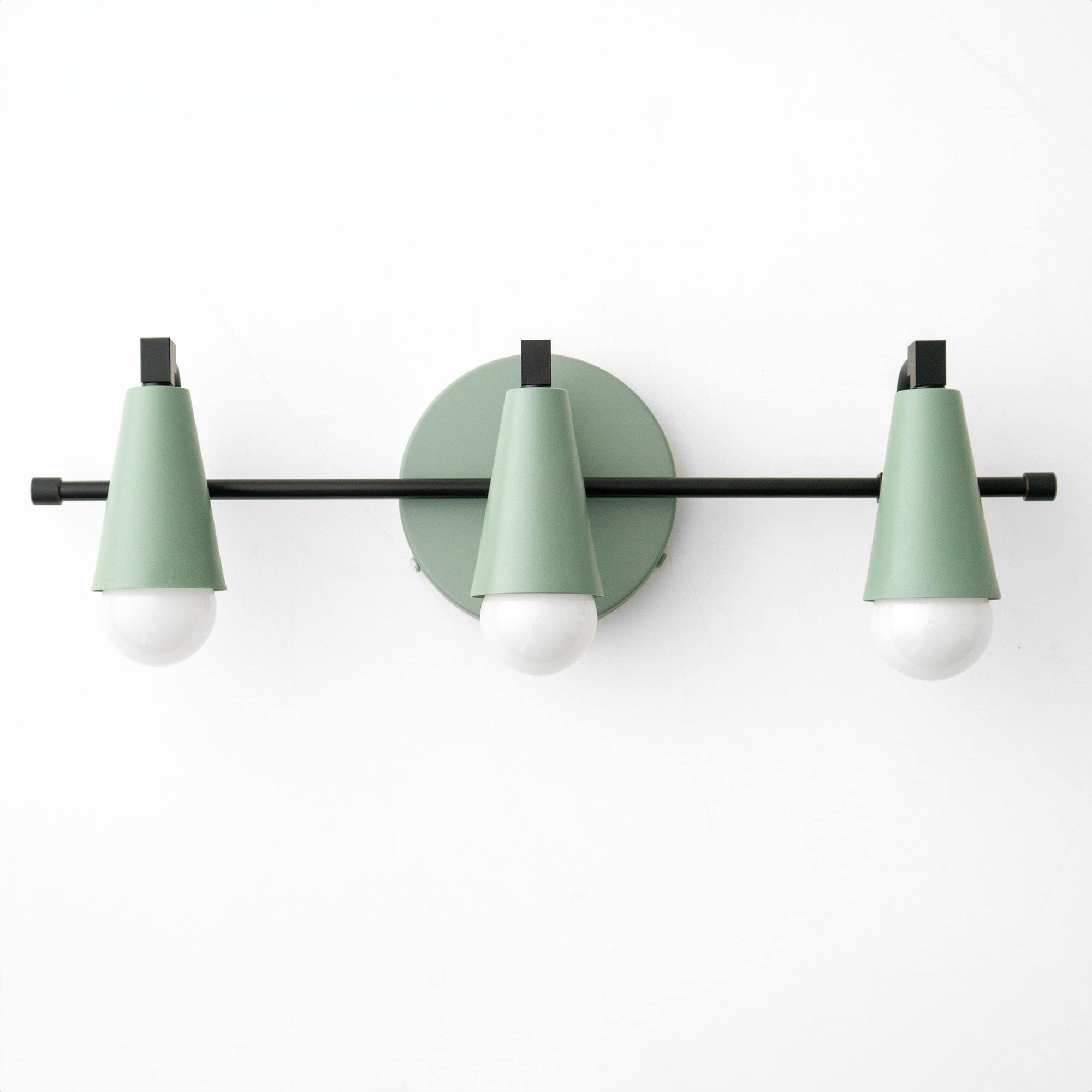 Three-bulb vanity light with matte black bar and muted green conical shades against white wall. - VANITY LIGHT MODEL NO. 8084