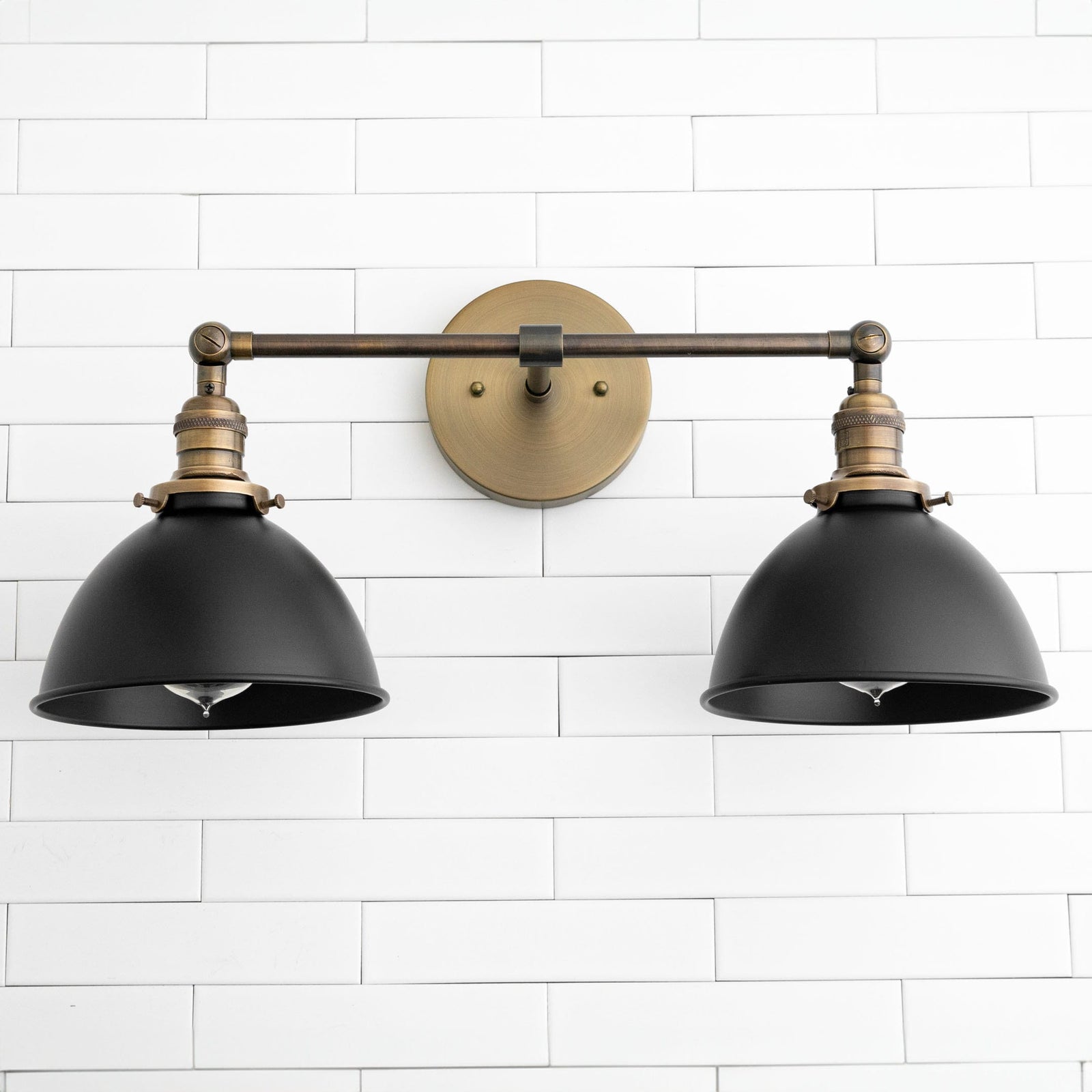 Two-light vanity sconce with black metal shades and antique brass fixtures mounted on white tile wall. - SCONCE MODEL NO. 8791