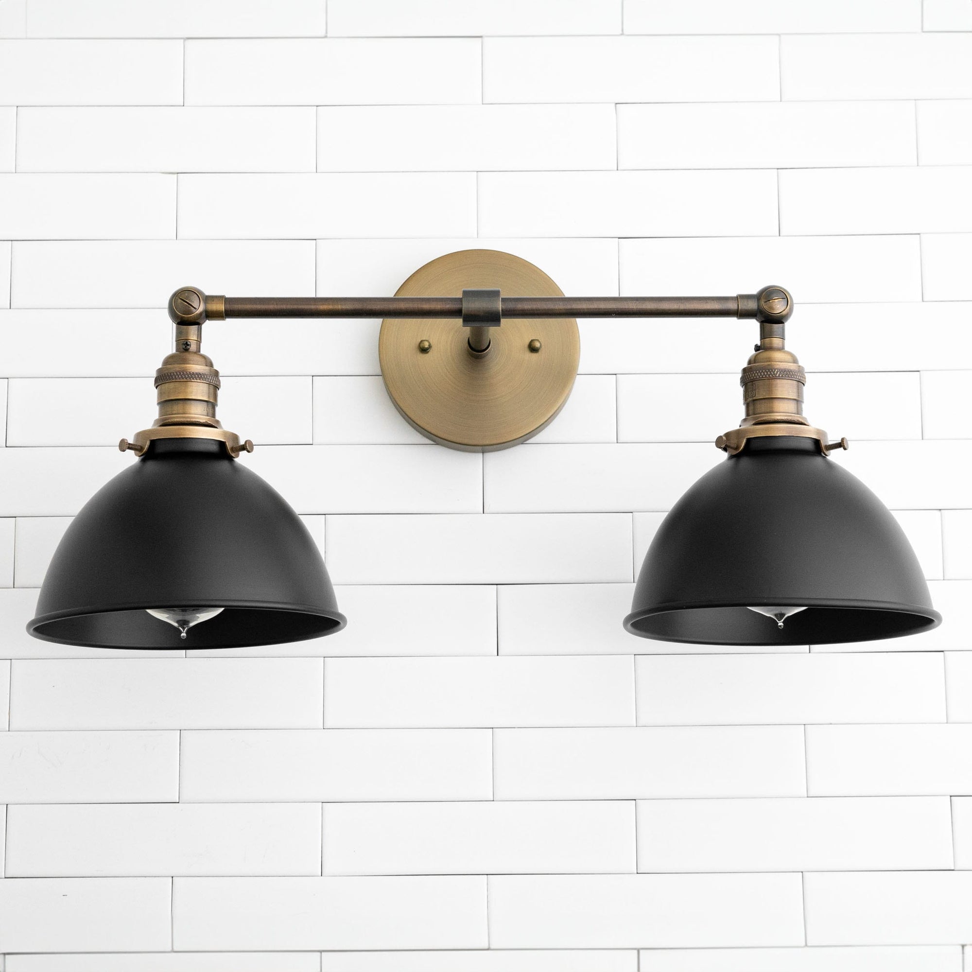 Two-light vanity sconce with black metal shades and antique brass fixtures mounted on white tile wall. - SCONCE MODEL NO. 8791