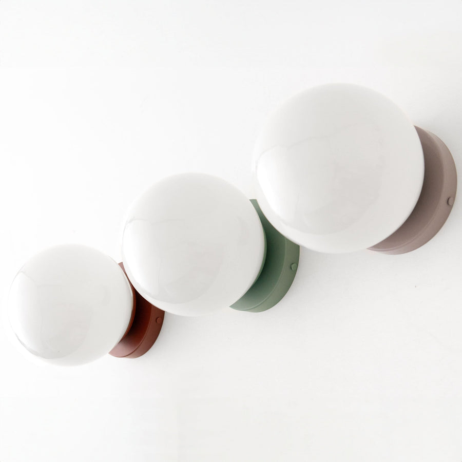 Three mid-century modern wall sconces with round white glass globes and flush mounts in brick red, green, and mauve finishes. - SCONCE MODEL NO. 3825