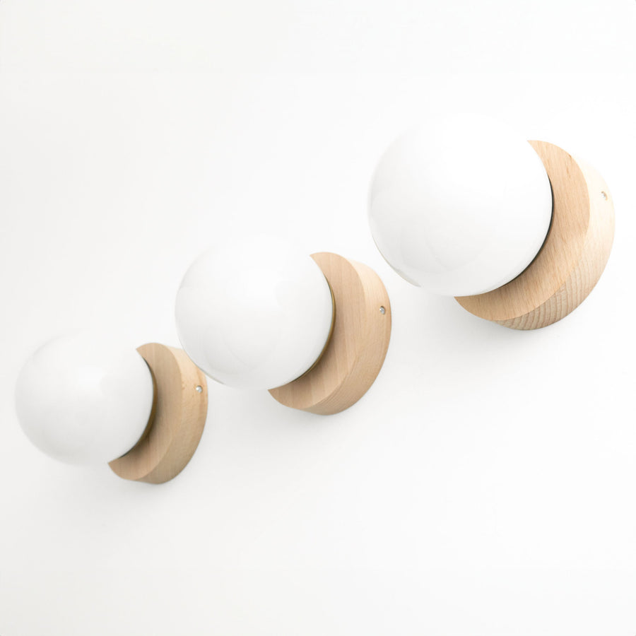 Three Scandinavian-style wall sconces with round frosted glass globes and natural beechwood bases mounted on a white wall. - SCONCE MODEL NO. 5719