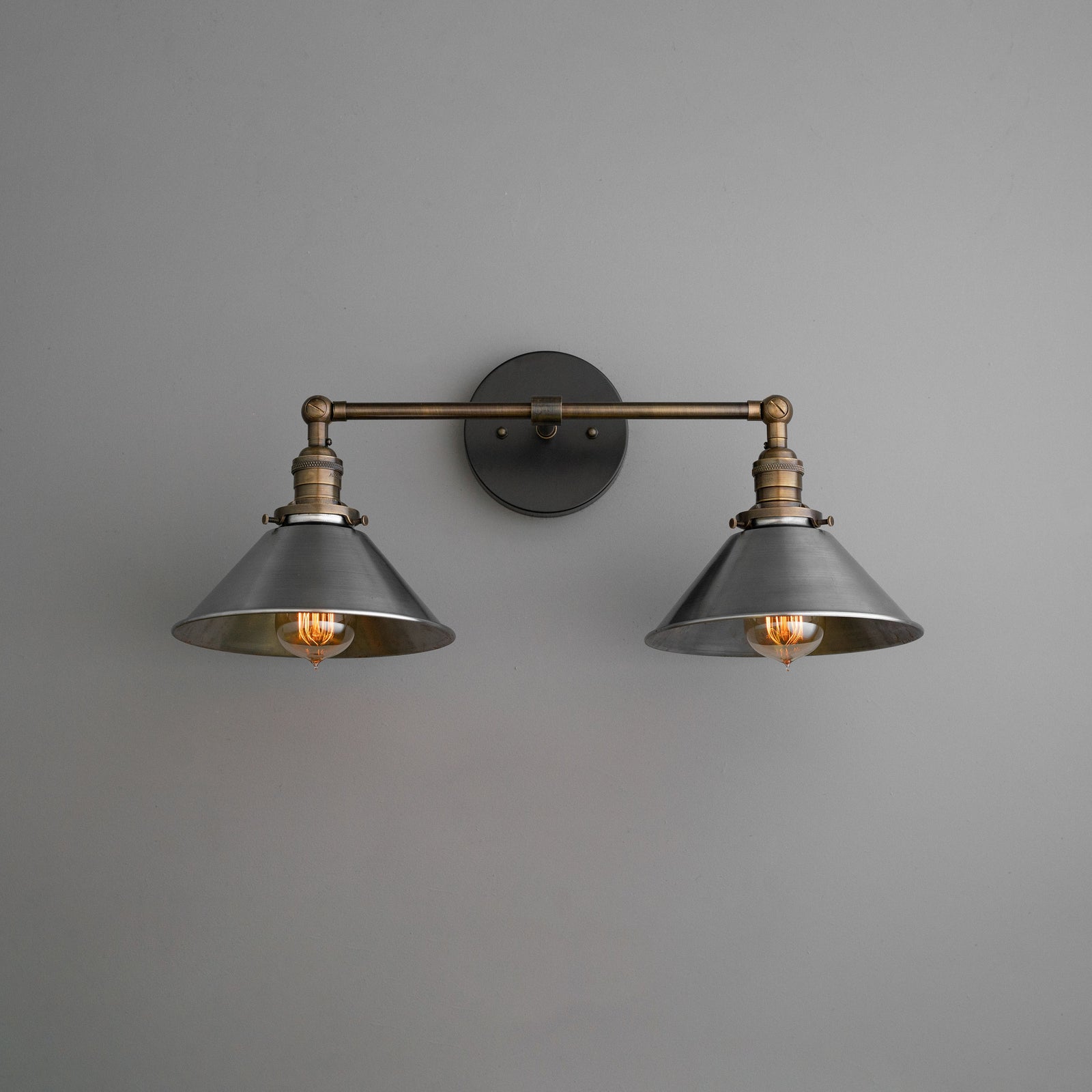 Industrial two-bulb vanity light with black metal shades and antique brass fixture mounted on gray wall. - VANITY LIGHT MODEL NO. 0799