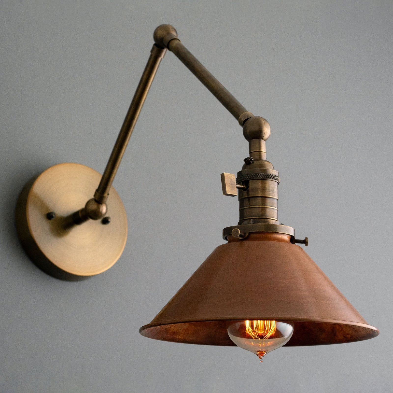 Adjustable industrial wall sconce with antique brass arm and wide copper shade showing exposed Edison bulb. - SCONCE MODEL NO. 6668