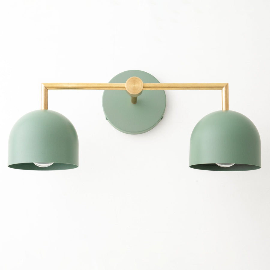 Art Deco vanity light with two green dome shades and raw brass horizontal bar and round wall mount. - VANITY LIGHT MODEL NO. 8432