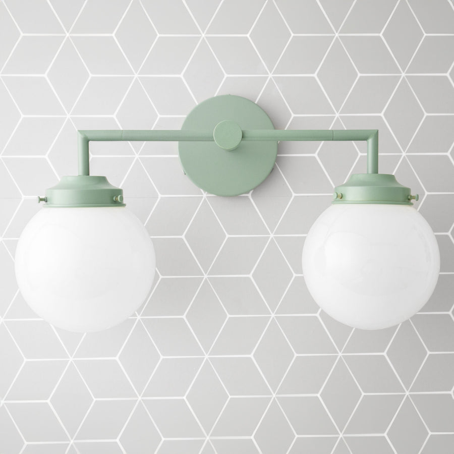 Green metal vanity light with two white globe bulbs and round wall mount. - VANITY LIGHT MODEL NO. 9500