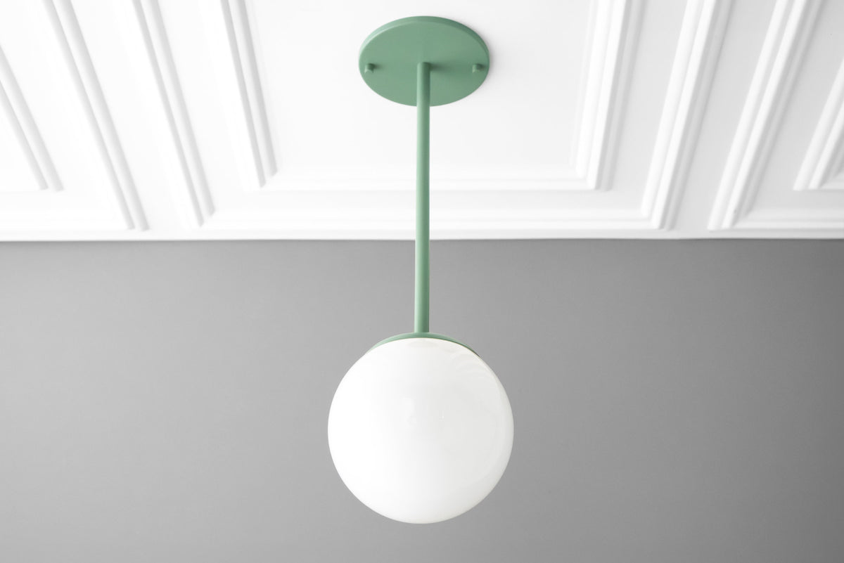 Mid-century modern pendant light with green metal rod and matte white globe shade suspended from paneled white ceiling. - PENDANT MODEL NO. 7559