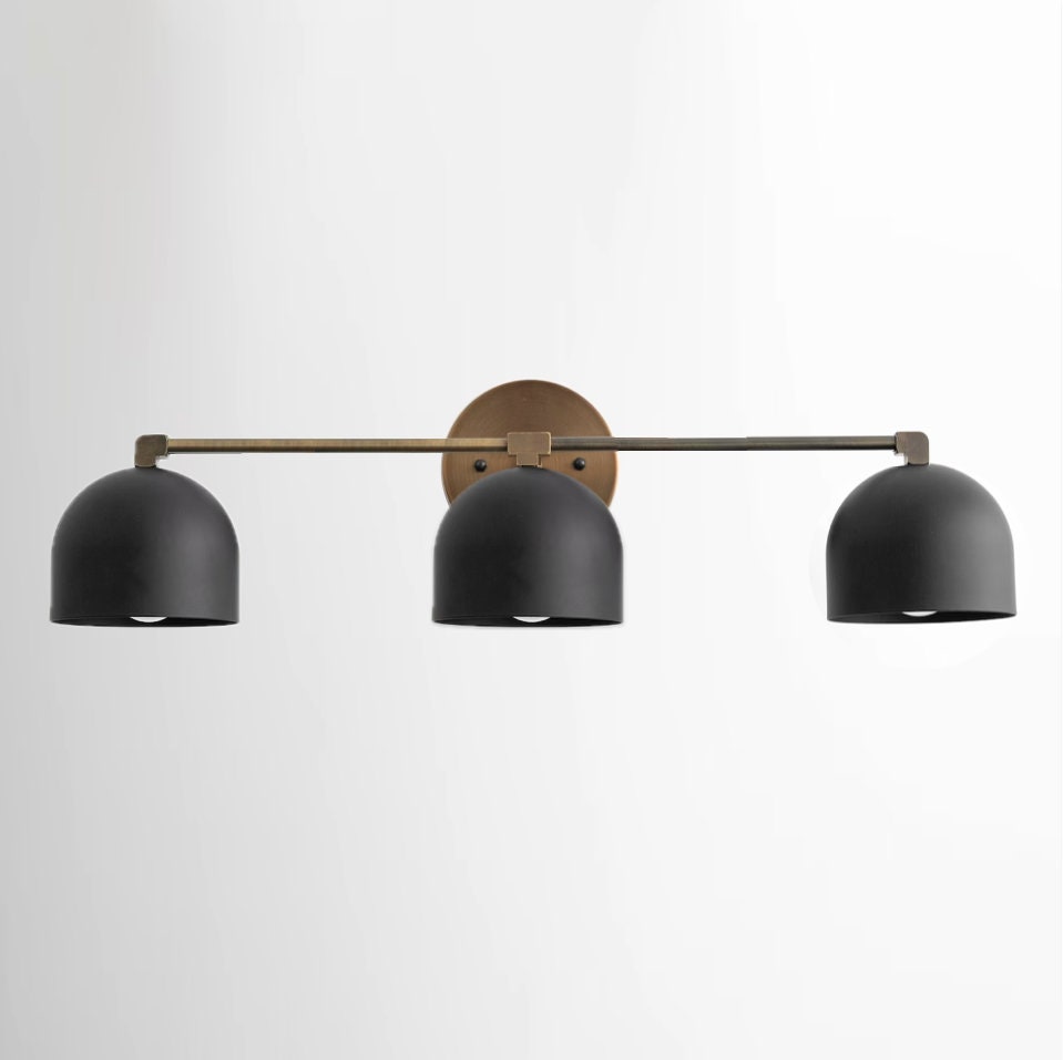 Mid-century modern vanity light with three matte black dome shades and antique brass horizontal bar and round wall mount. - VANITY LIGHT MODEL NO. 7565