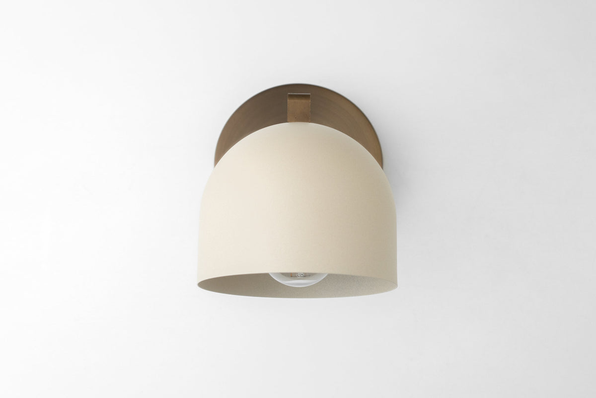 Wall sconce with cream dome shade and antique brass circular base mounted on white wall. - SCONCE MODEL NO. 8704