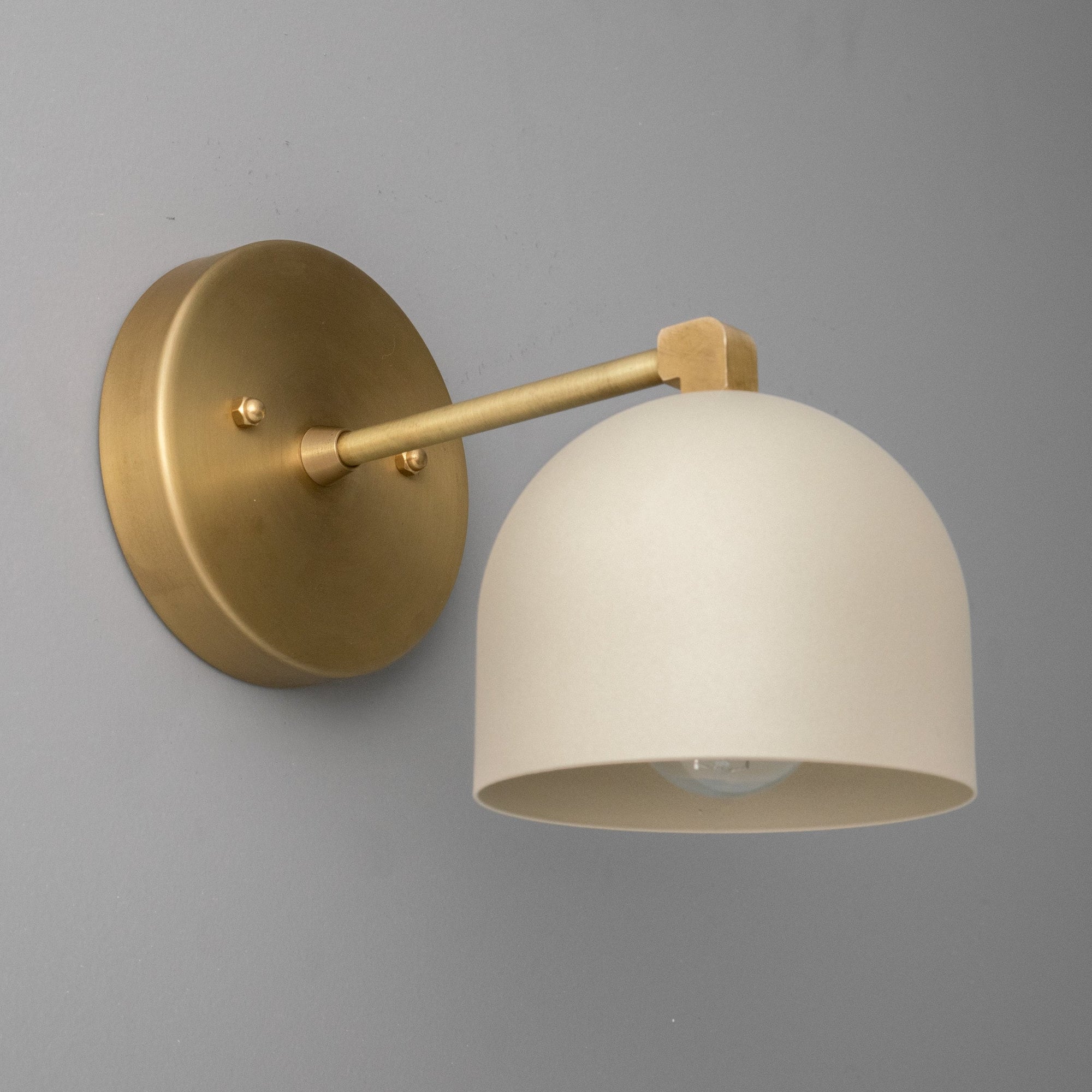 Wall-mounted sconce with brass finish and smooth cream dome shade against gray wall. - SCONCE MODEL NO. 8704