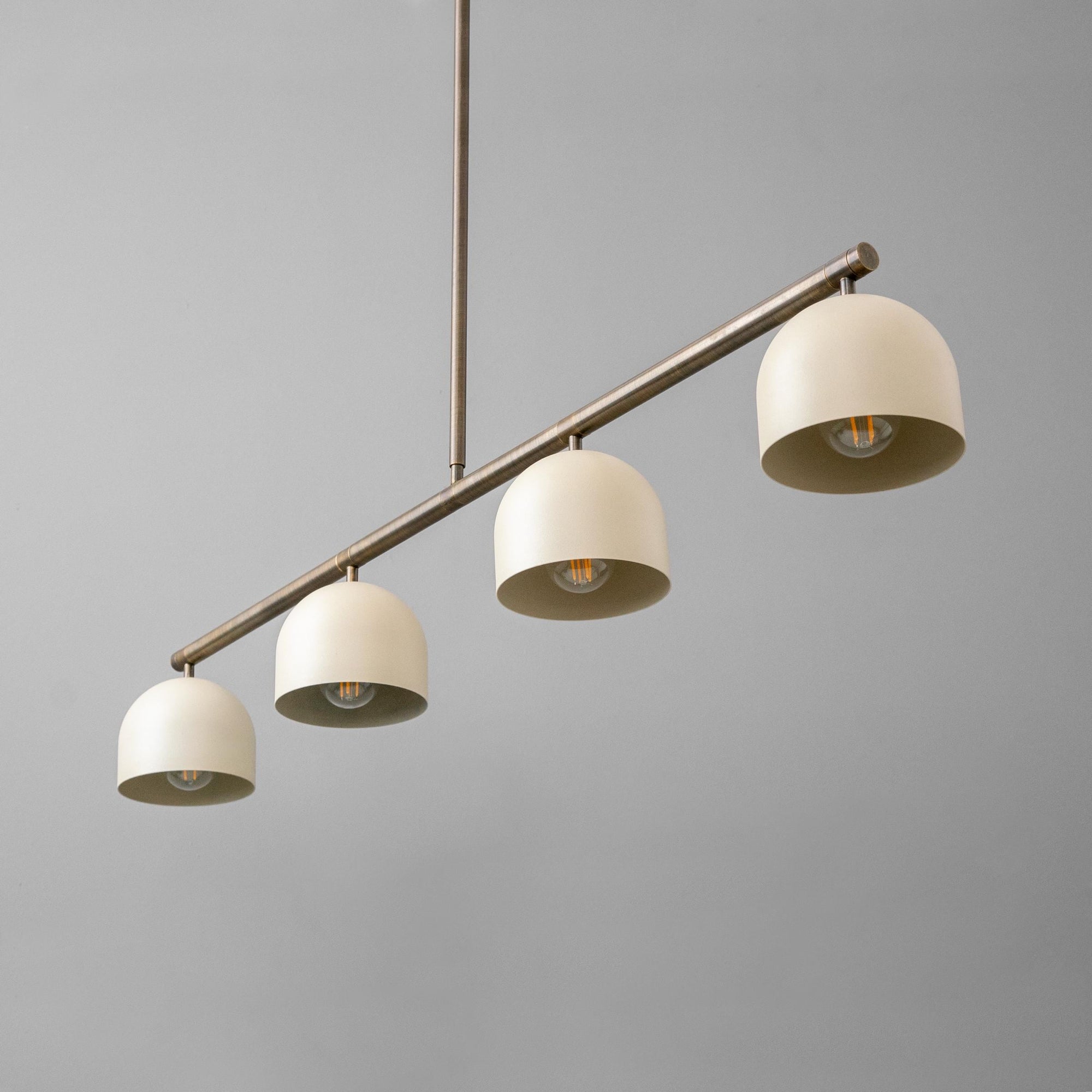 Linear chandelier with four cream dome shades on antique brass rod suspension. - CHANDELIER MODEL NO. 7998