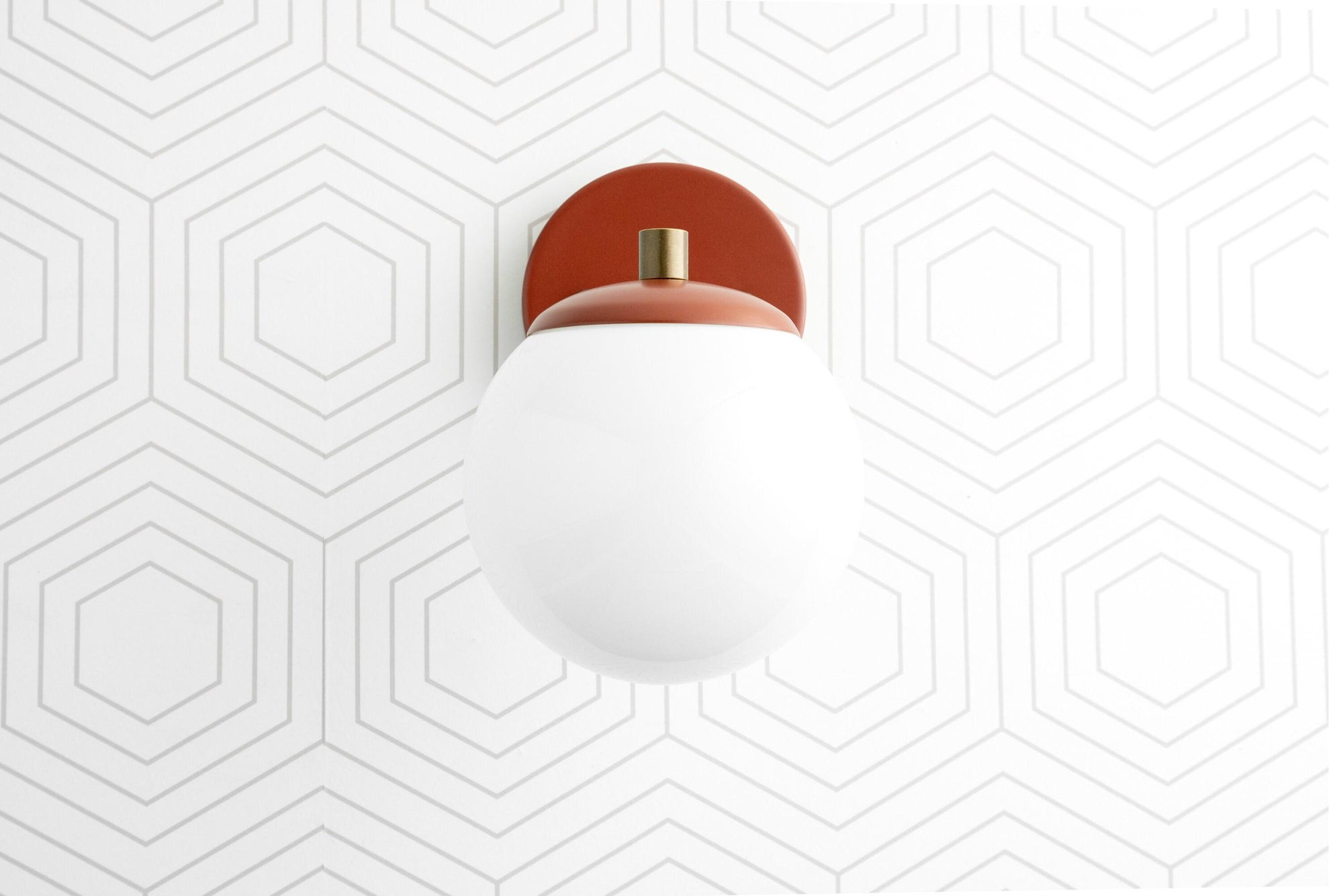 Semi-flush wall sconce with white globe and matte red circular brass base on geometric patterned wall. - SCONCE MODEL NO. 5524