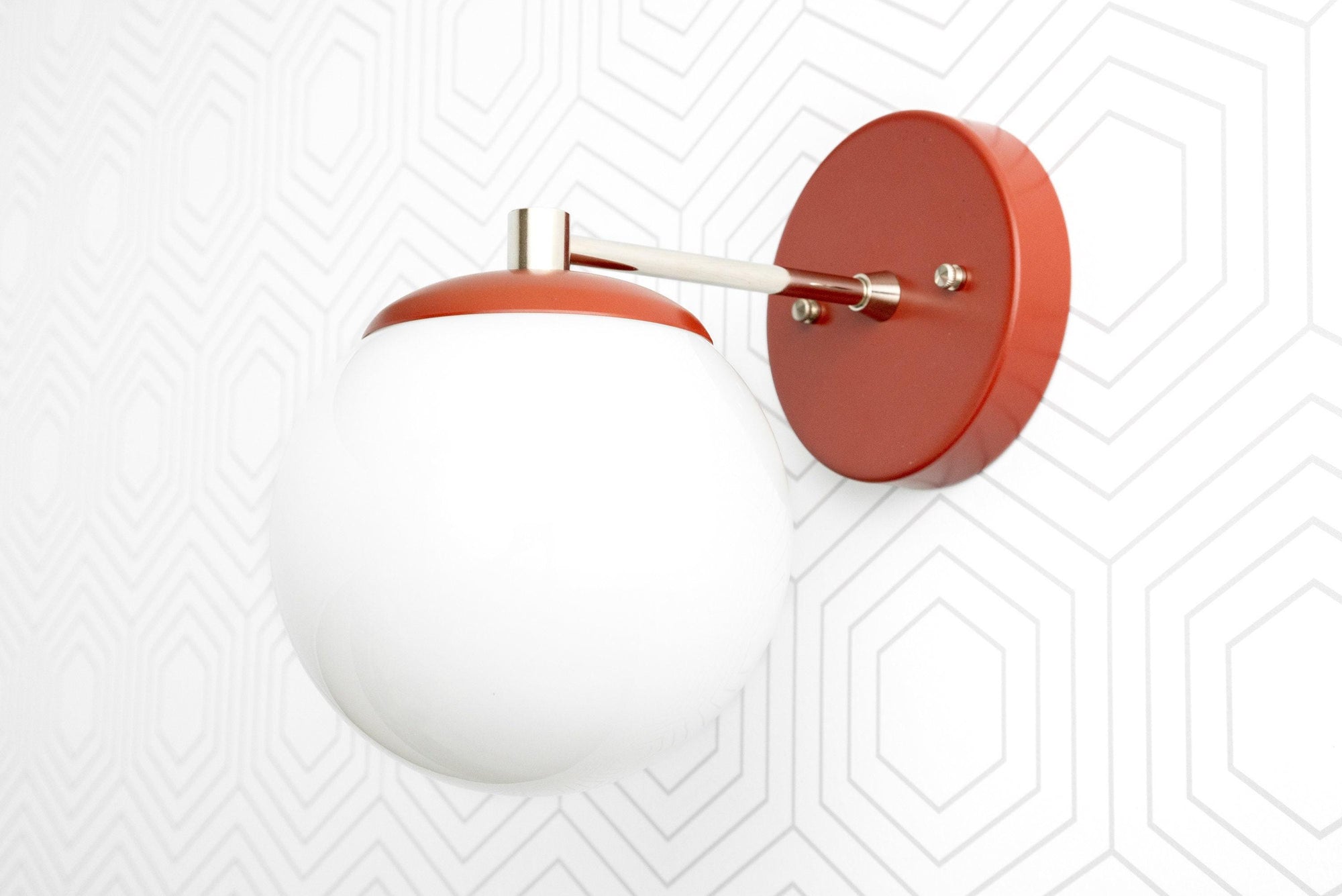 Matte white globe sconce with red brass mount and arm on geometric patterned white wall. - SCONCE MODEL NO. 5524