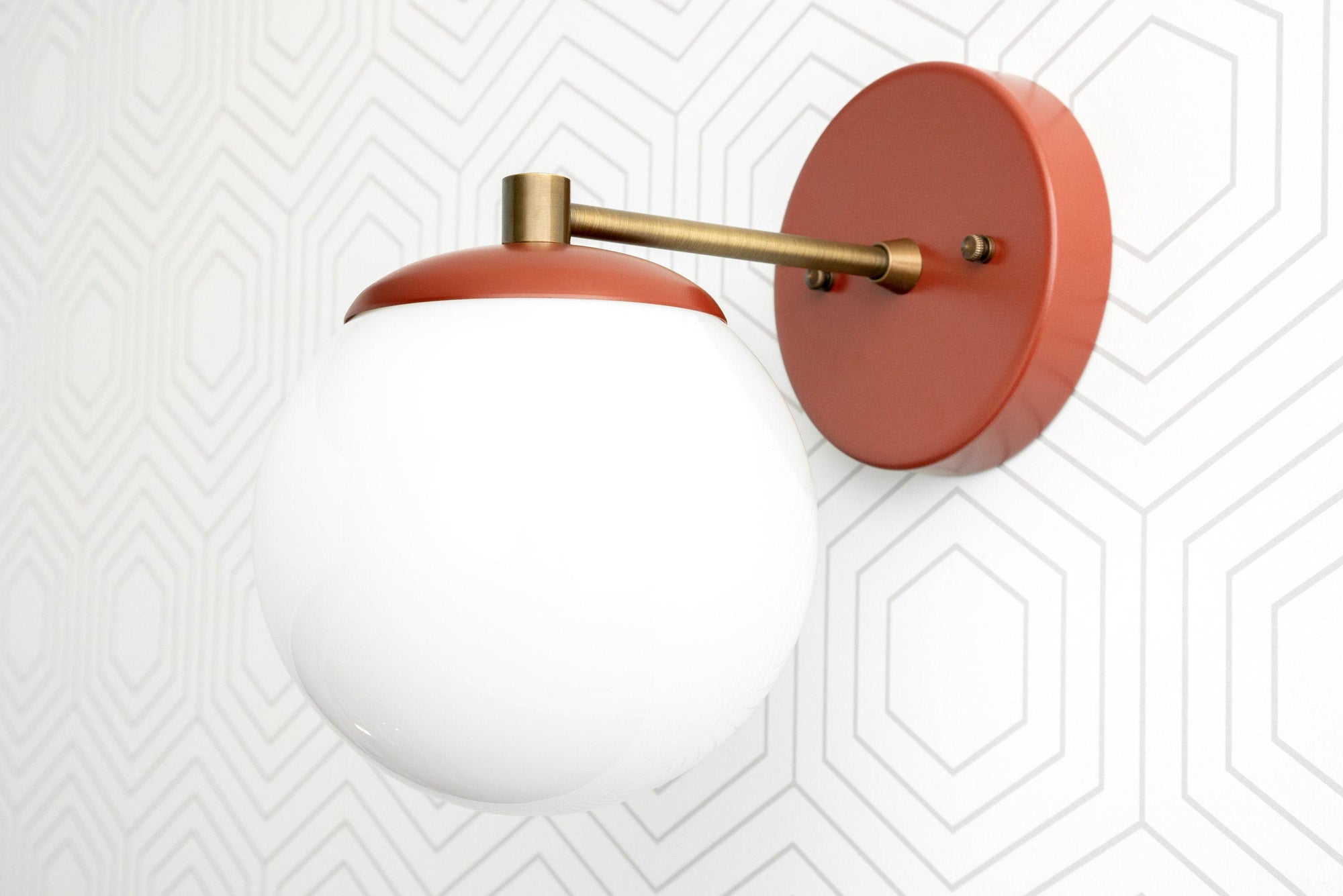 Matte terracotta wall sconce with frosted white glass globe and brass arm mount on geometric white wall. - SCONCE MODEL NO. 5524