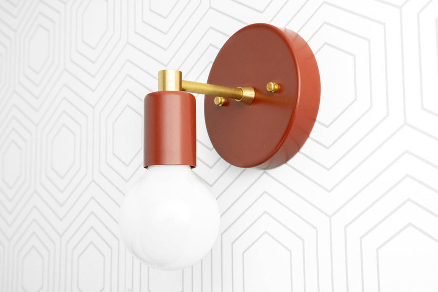 Scandinavian style wall sconce with raw brass arm and matte red circular base holding a bare bulb. - SCONCE MODEL NO. 9036