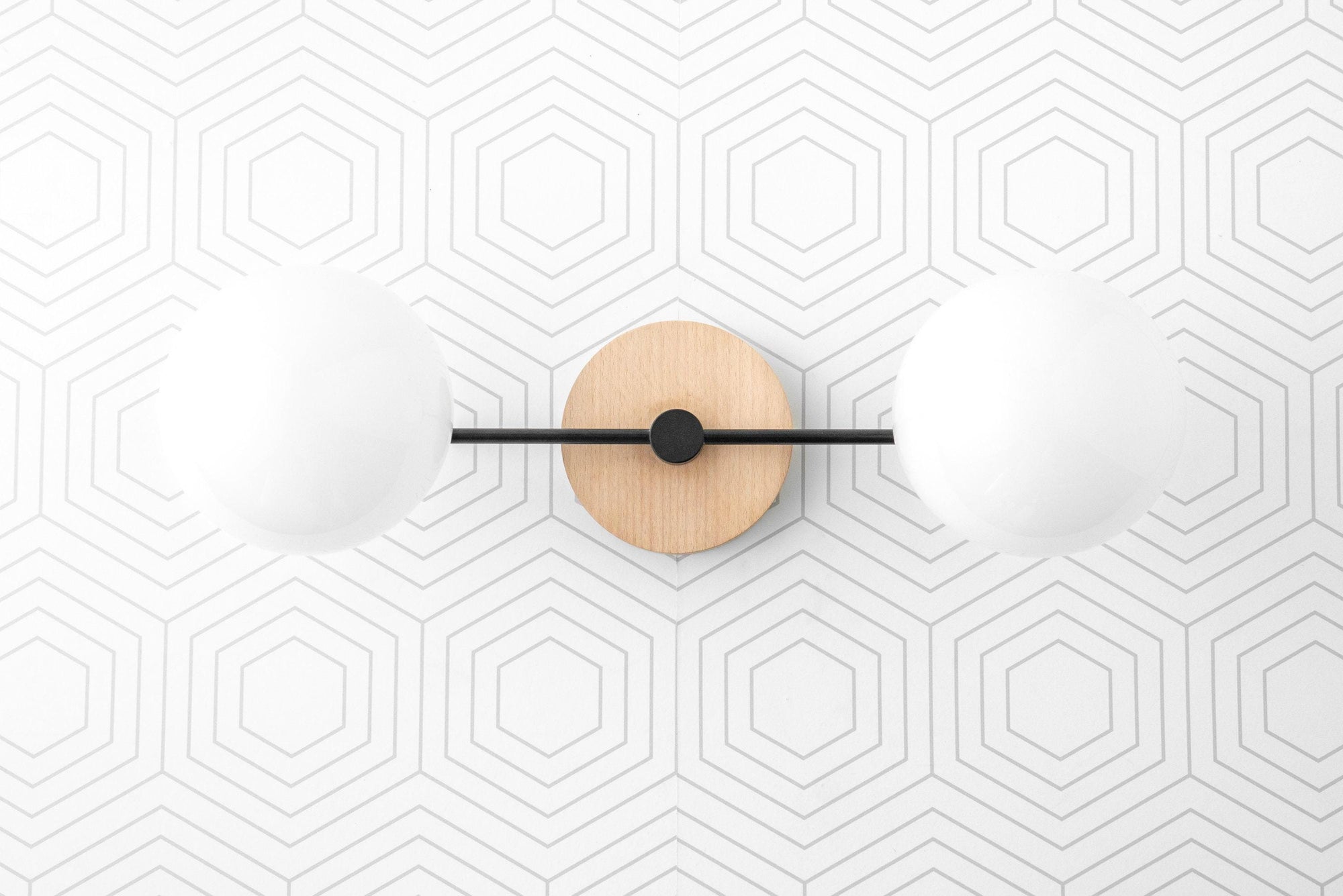 Two-globe vanity light with matte black metal arms and round natural wood wall mount on geometric wallpaper background. - VANITY LIGHT MODEL NO. 9474