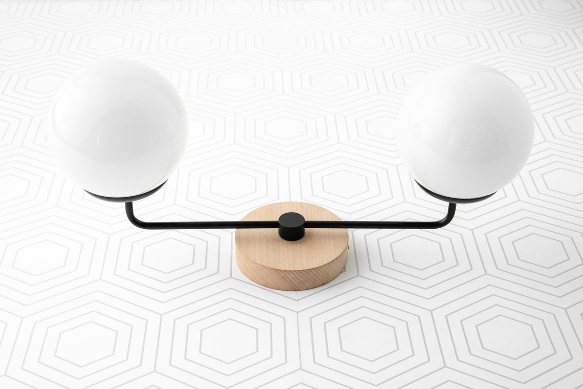 Two-globe vanity light with matte black arms and natural wood circular base on white geometric tile background. - VANITY LIGHT MODEL NO. 9474