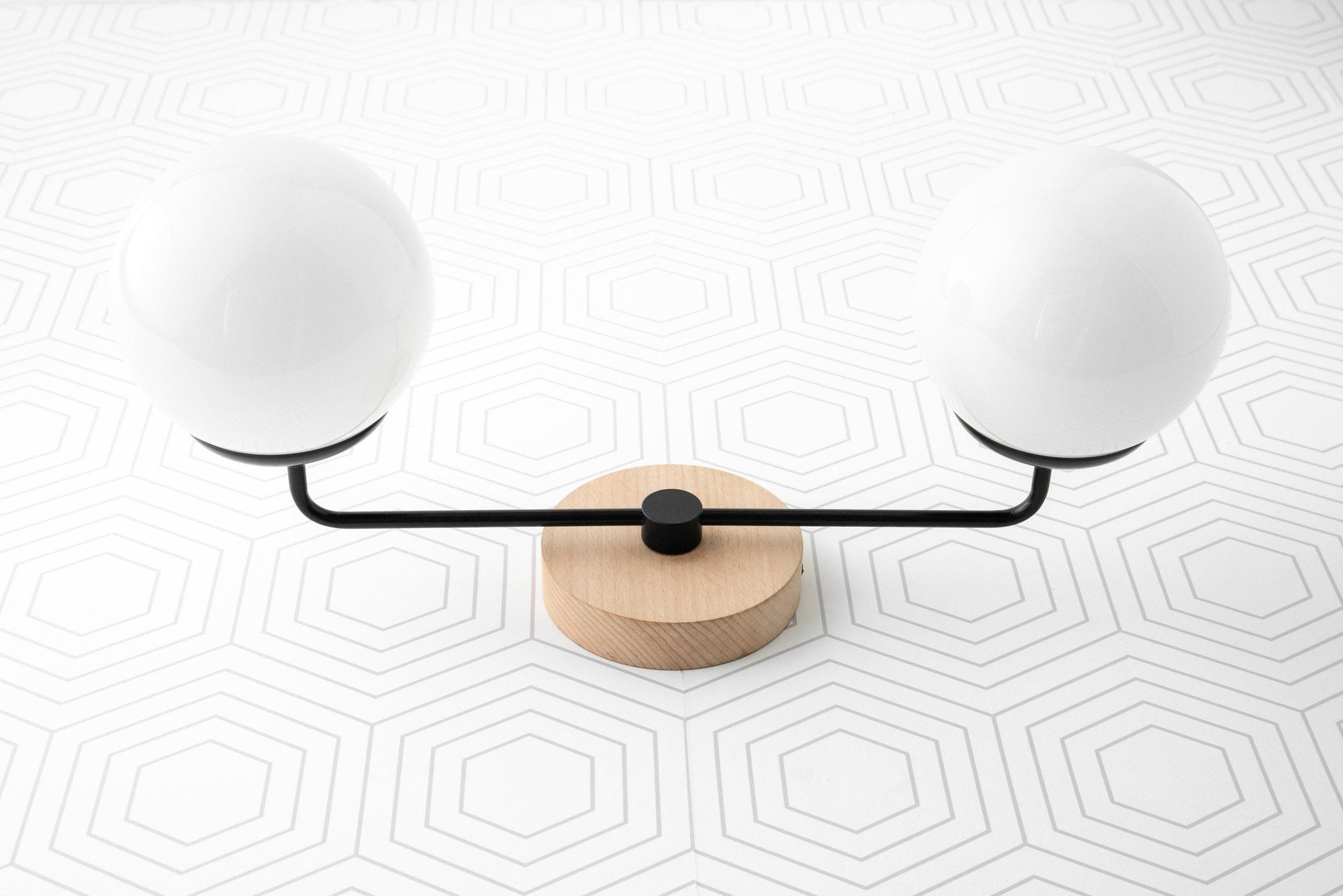 Two-globe vanity light with matte black arms and natural wood circular base on white geometric tile background. - VANITY LIGHT MODEL NO. 9474