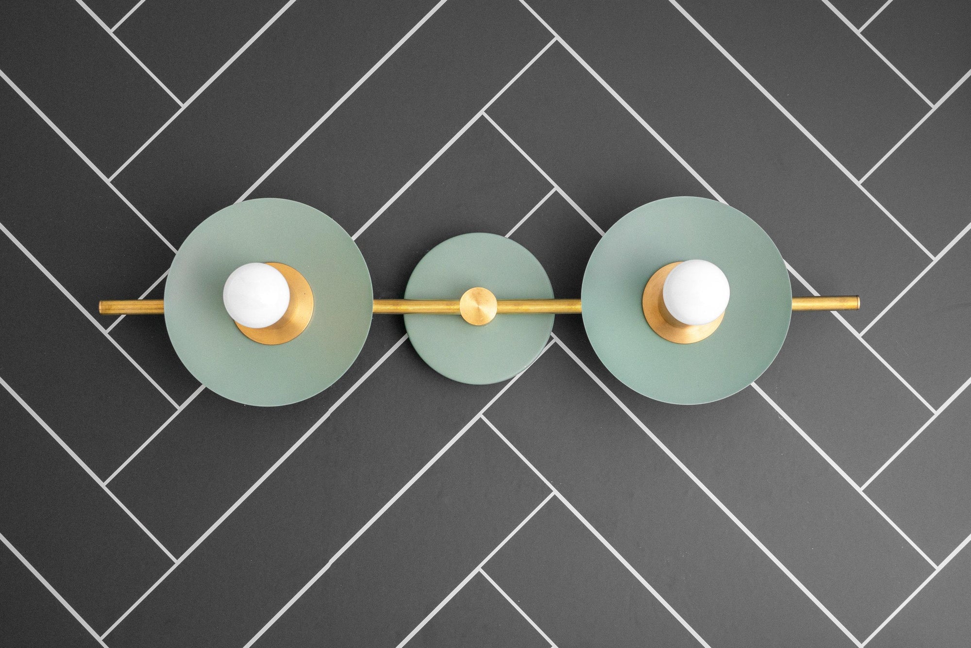 Raw brass vanity light with two green circular shades and exposed bulbs on dark tiled background. - VANITY LIGHT MODEL NO. 8151