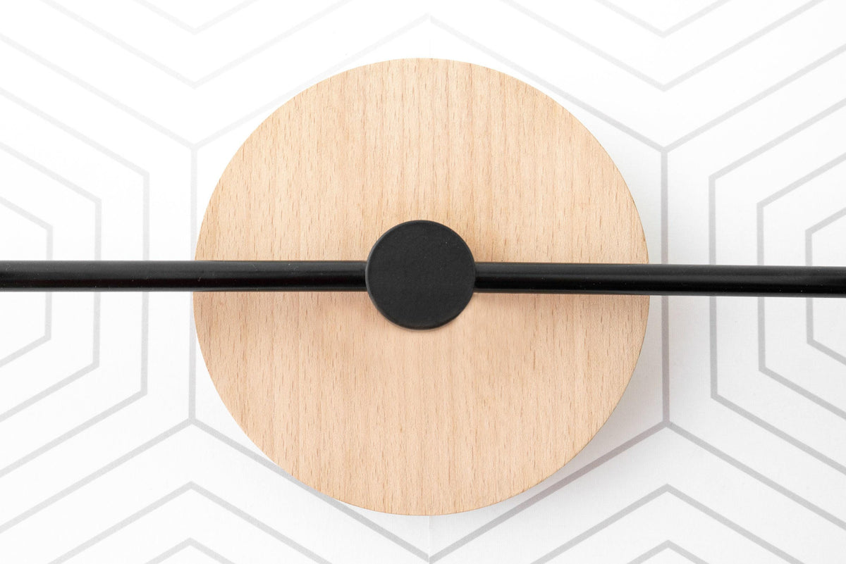 Vanity light with black metal bar mounted on round natural wood backplate against geometric white wall. - VANITY LIGHT MODEL NO. 9474