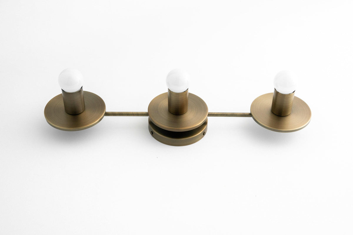 Three-bulb antique brass vanity light with round bases and exposed white bulbs. - VANITY LIGHT MODEL NO. 5708