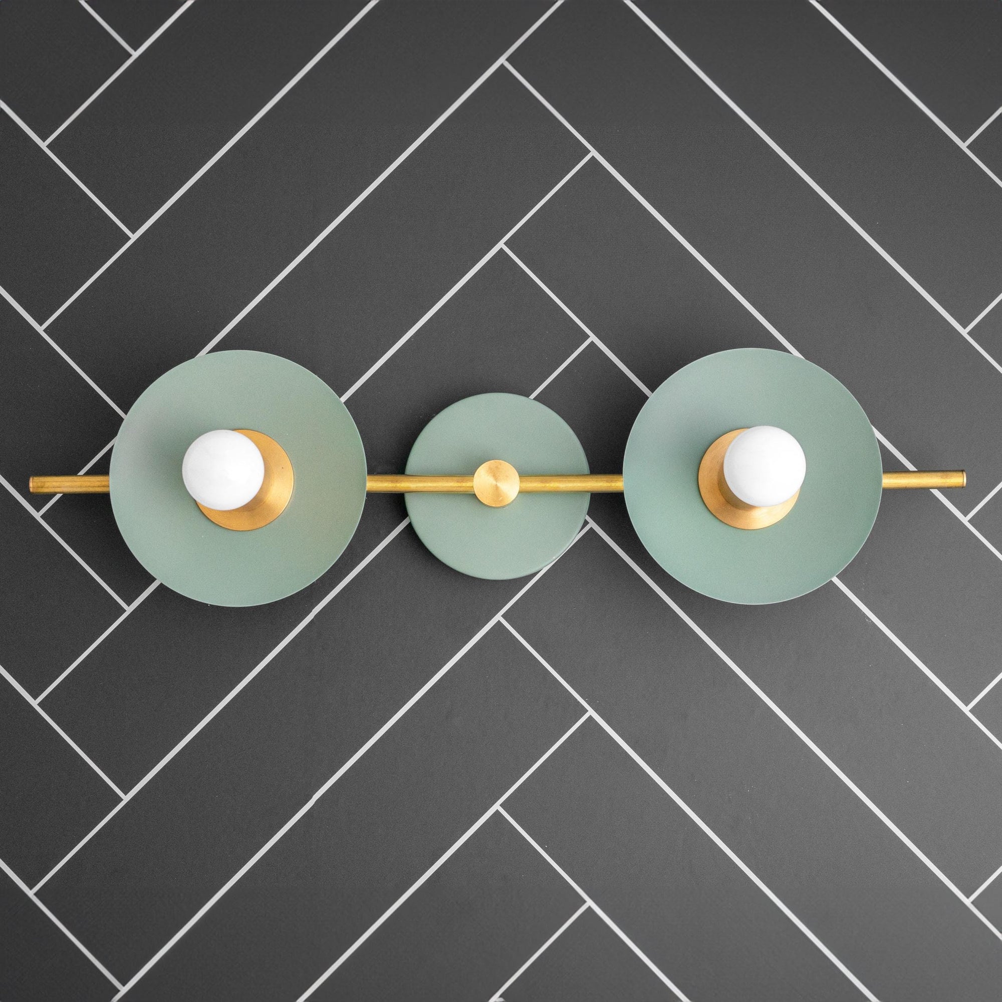 Raw brass vanity light with three circular green backplates and exposed bulbs on black tiled wall. - VANITY LIGHT MODEL NO. 8151