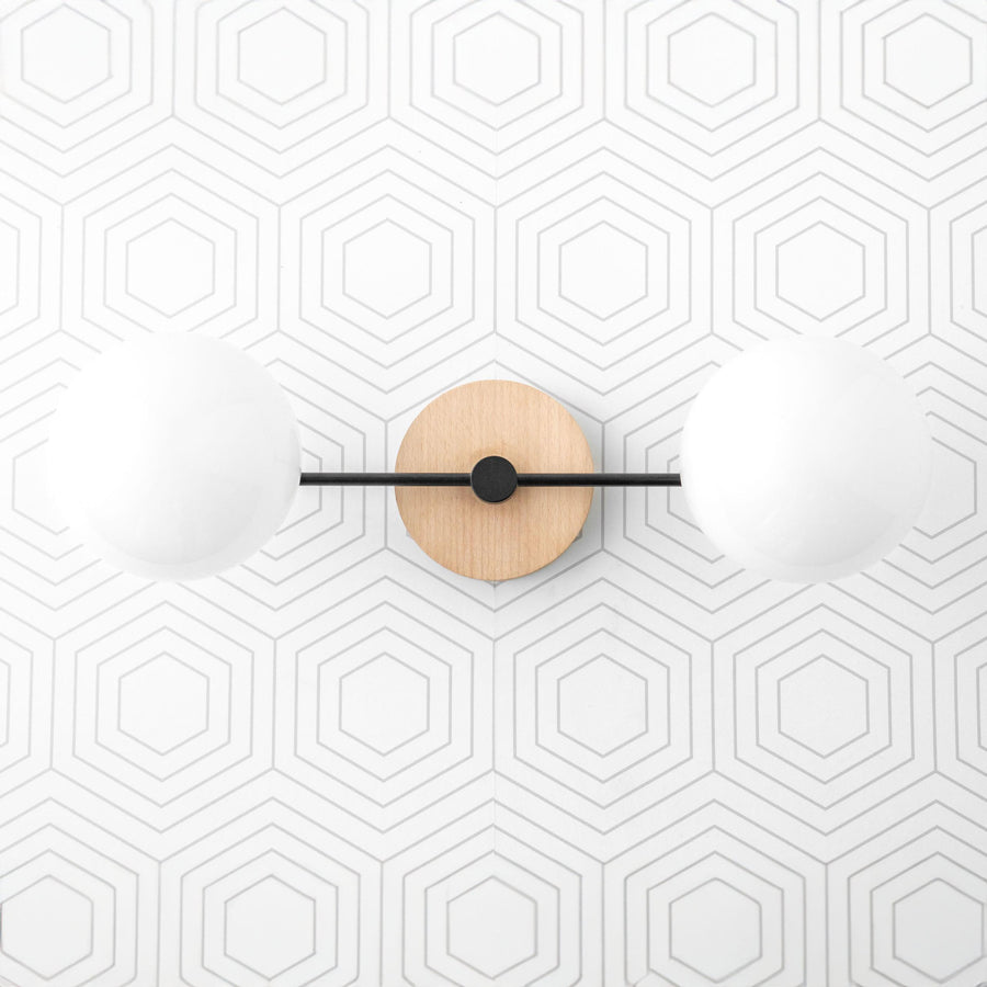 Two-globe vanity light with matte black metal arms and natural wood circular base on hexagonal tiled wall. - VANITY LIGHT MODEL NO. 9474