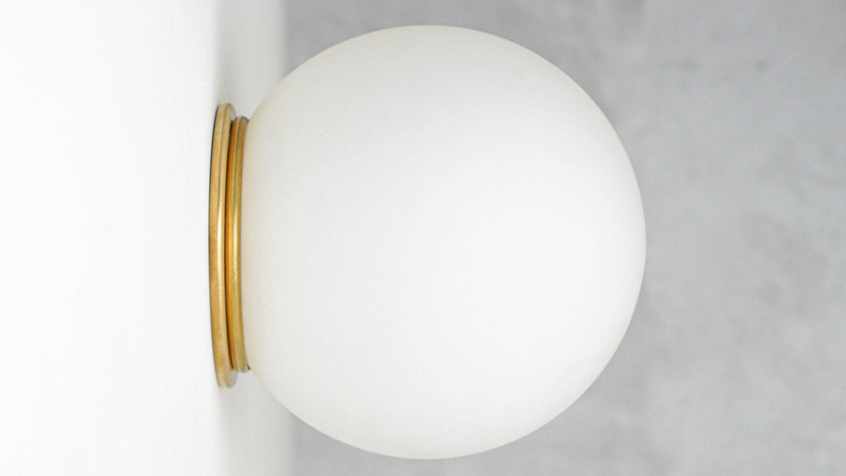 Wall-mounted sconce with round white glass globe and raw brass base flush against a white wall. - SCONCE MODEL NO. 4037