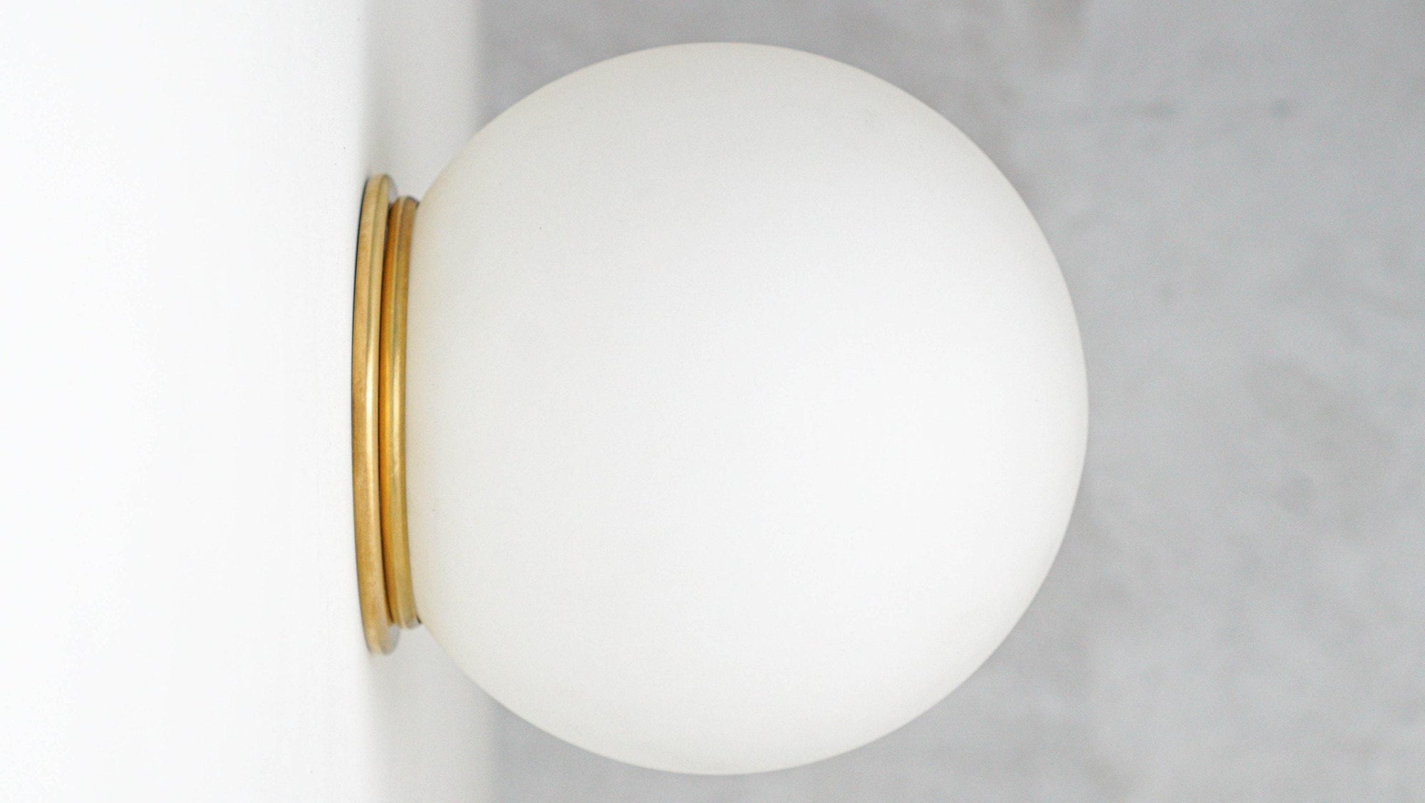 Wall-mounted sconce with round white glass globe and raw brass base flush against a white wall. - SCONCE MODEL NO. 4037