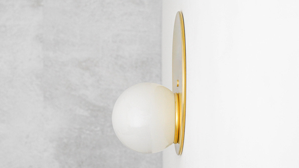 Mid-century modern black and brass wall sconce with a frosted globe shade mounted on white wall. - SCONCE MODEL NO. 6703