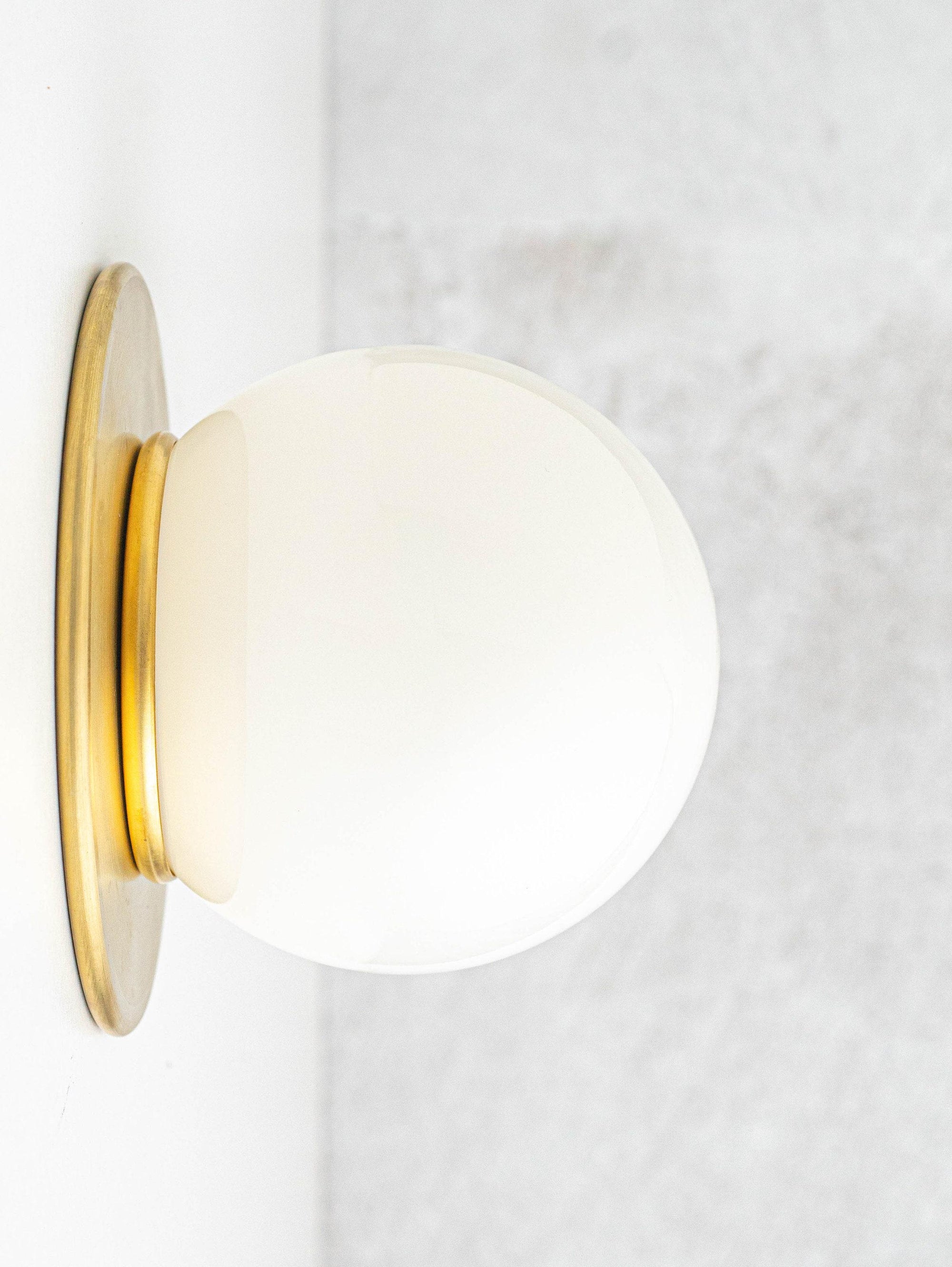 Mid-century modern wall sconce with frosted globe shade and raw brass base flush mounted on light gray wall. - SCONCE MODEL NO. 9364